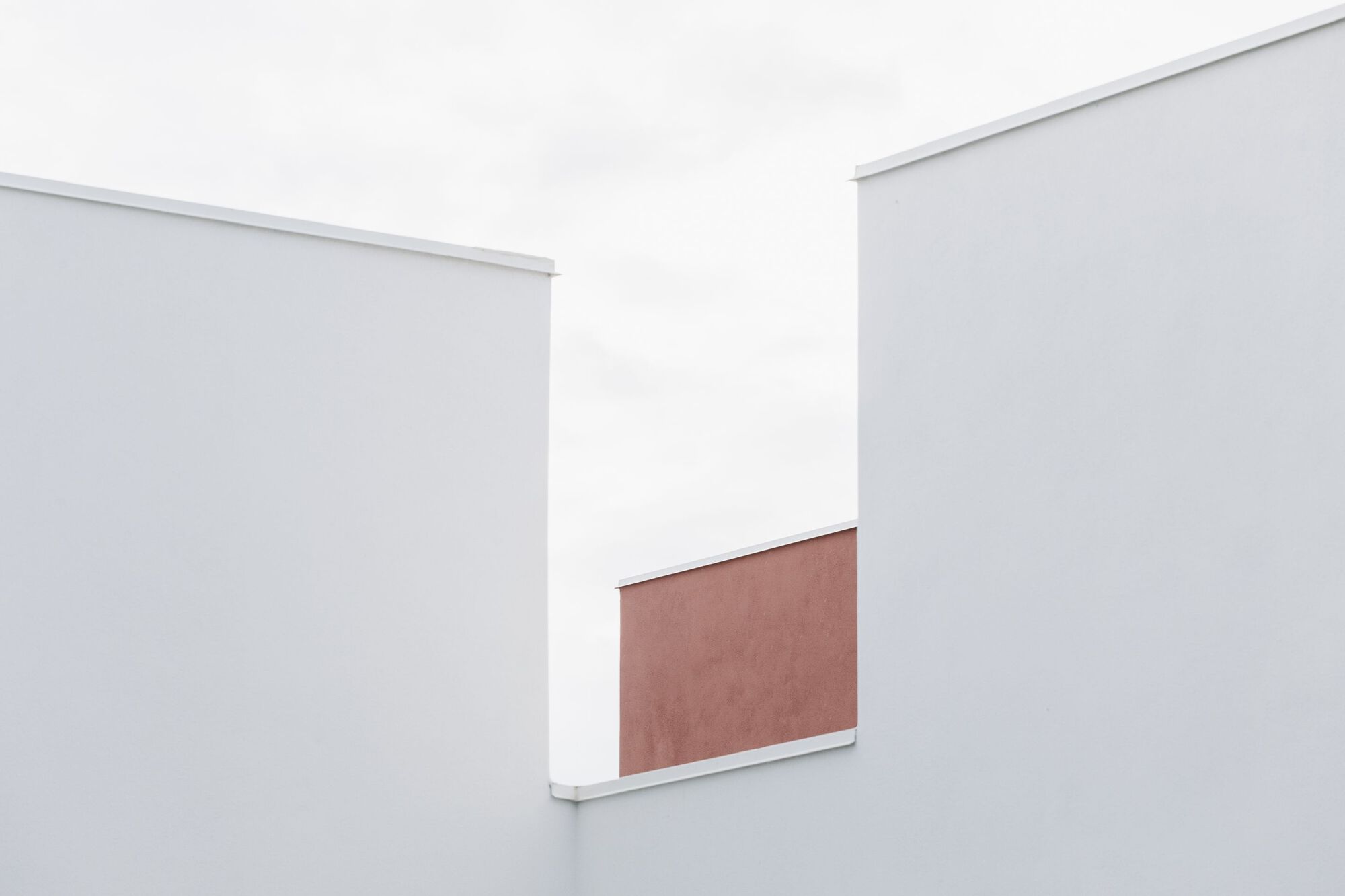 Abstract composition of white volumes with a terracotta panel glimpsed between them under diffused daylight