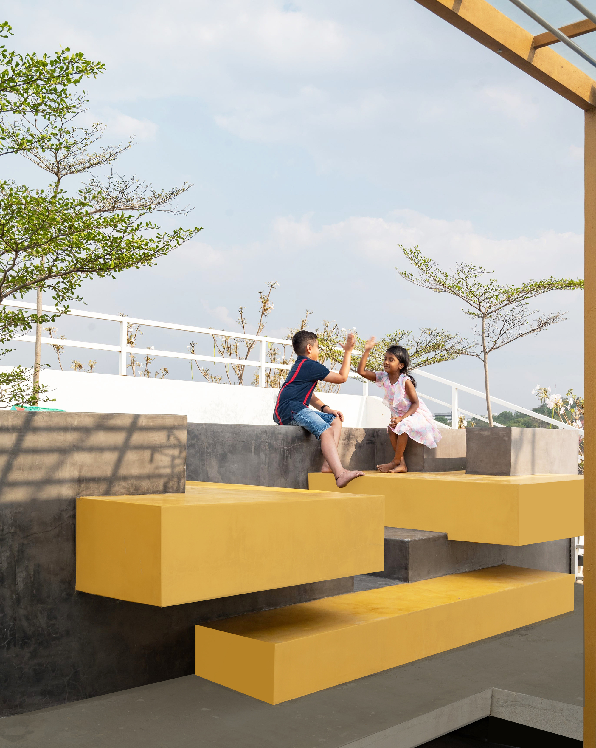 Cantilevered yellow steel stairs with two children playing under open sky and scattered clouds