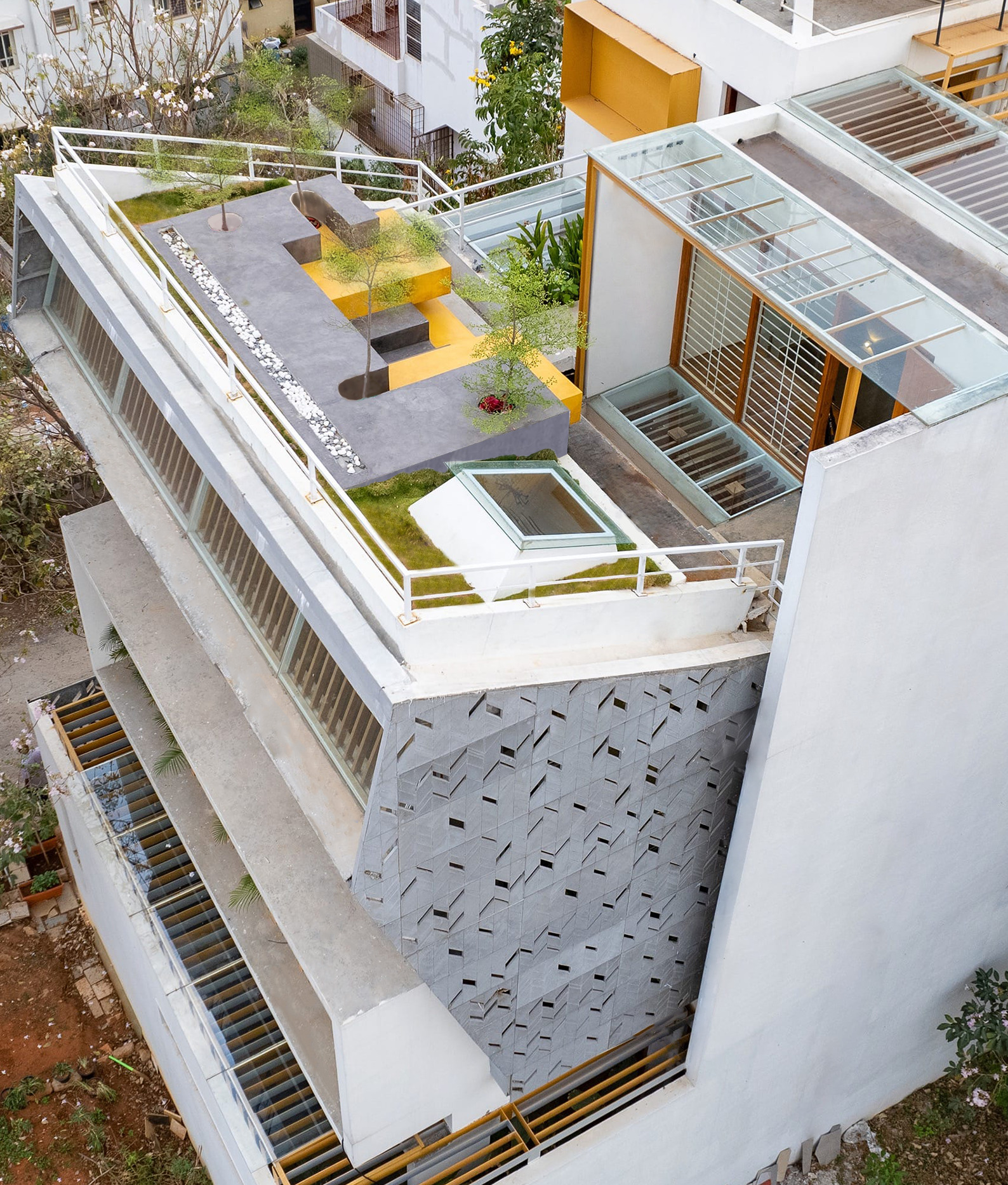 Aerial view of the multi-level residence with rooftop garden, yellow accents, and perforated courtyard paving