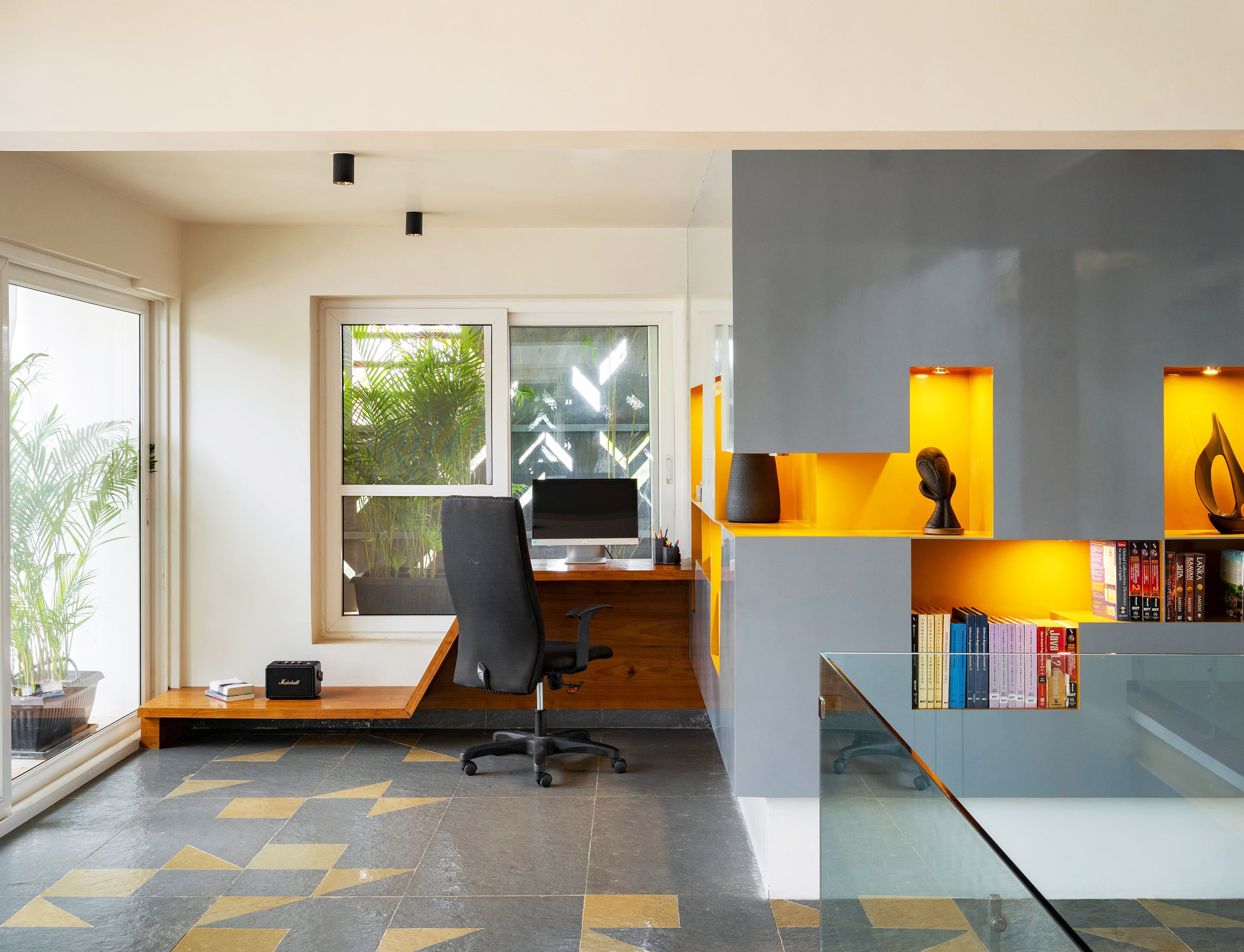 Work area with grey tile flooring, yellow wall niches, built-in desk, and perforated metal screen beyond the window