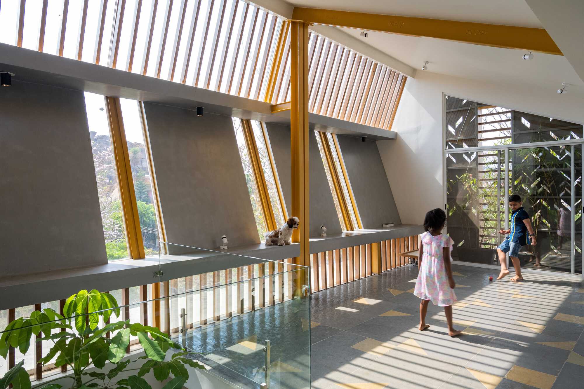 Upper hall with angled timber louvre clerestory casting striped light on two children walking across grey tiles