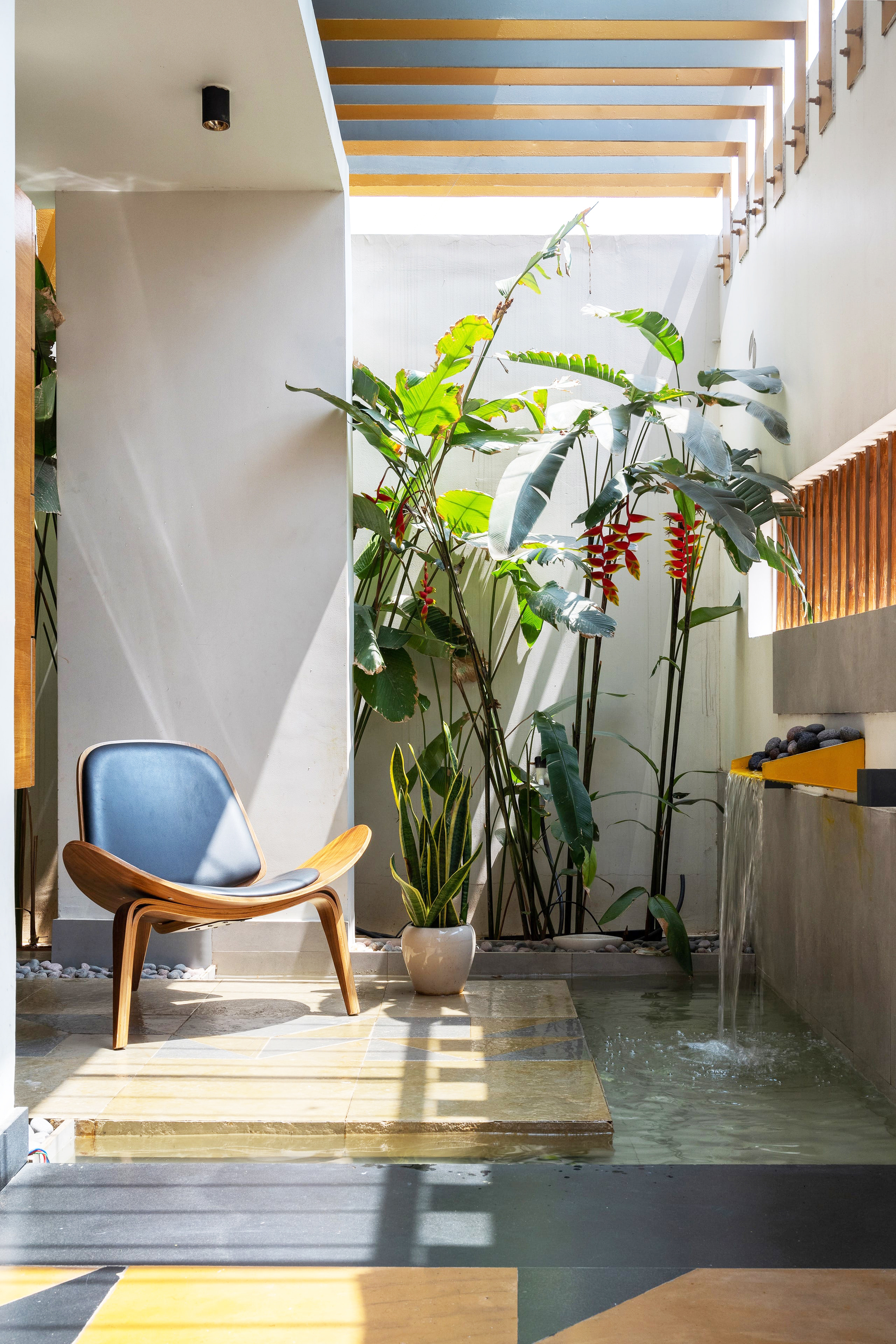 Double-height courtyard with planted bed, water channel, and timber battens filtering sunlight from above