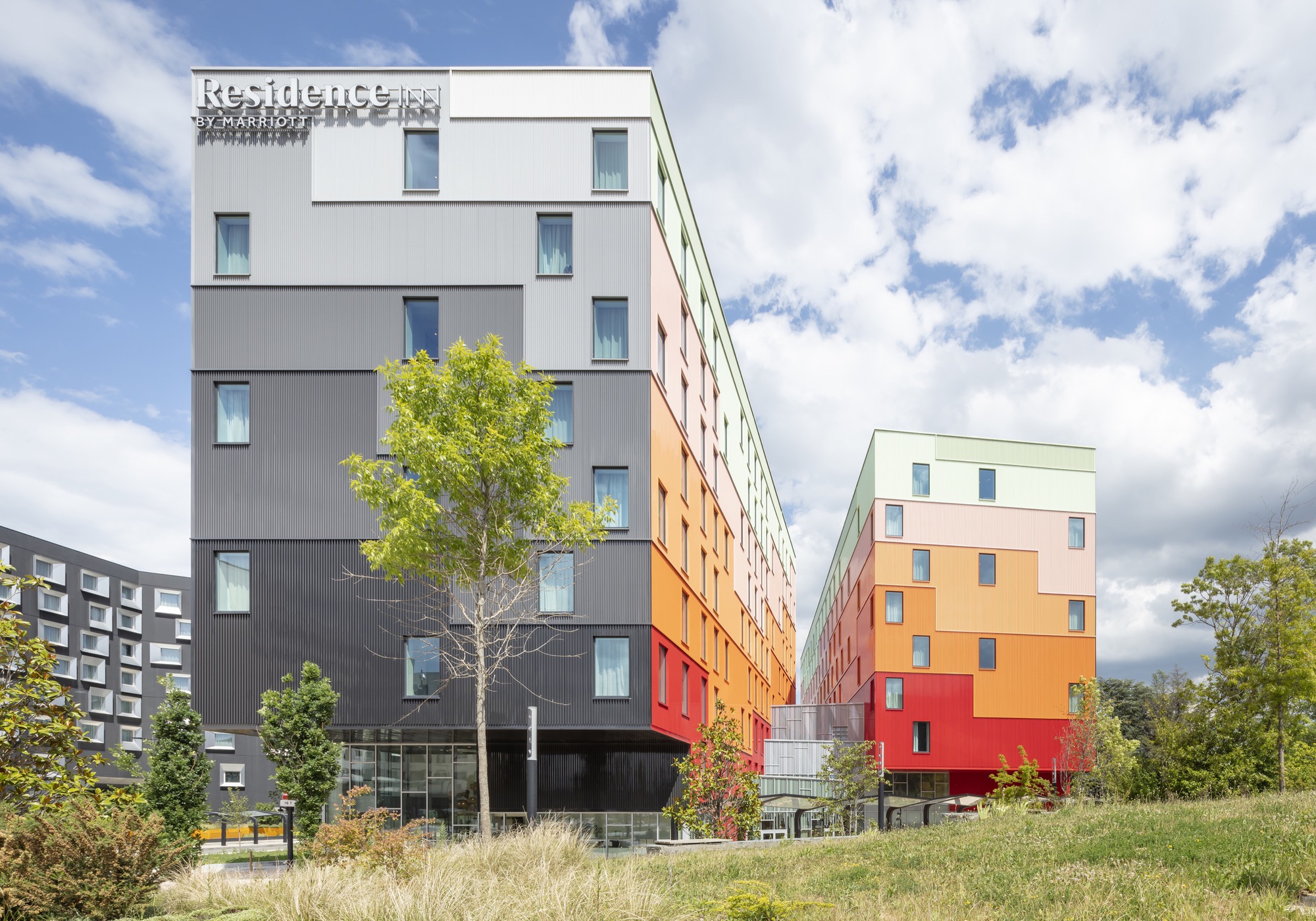 Two residential blocks with color-shifting facades separated by a narrow courtyard with young trees