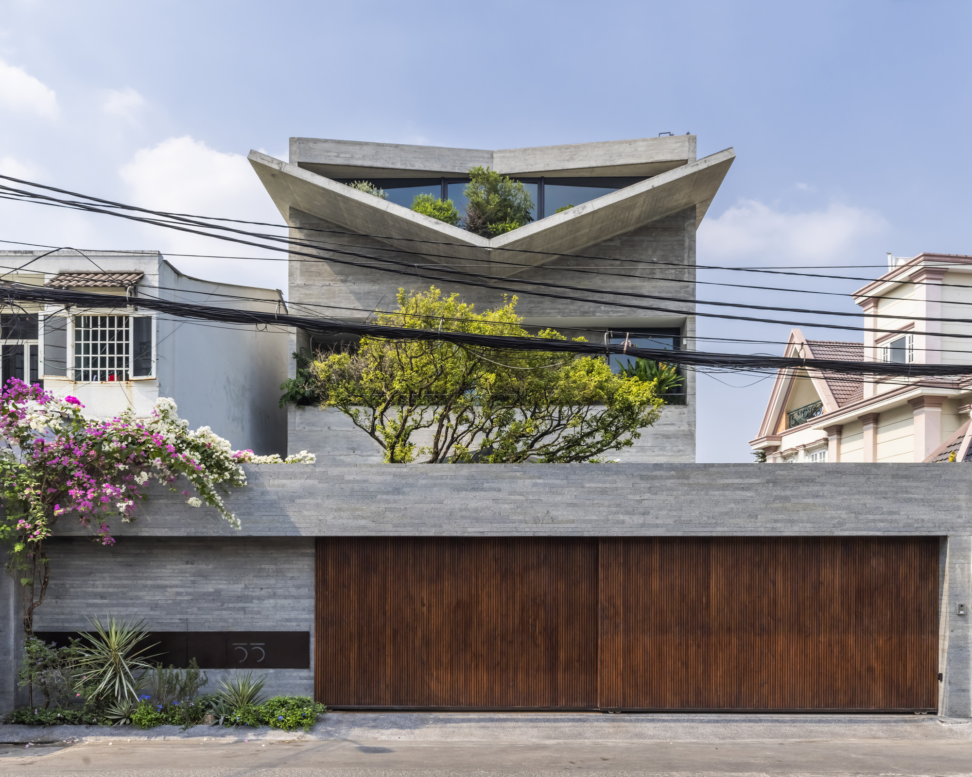 Street view of the board-formed concrete facade with folded roof planes and vertical wood garage door