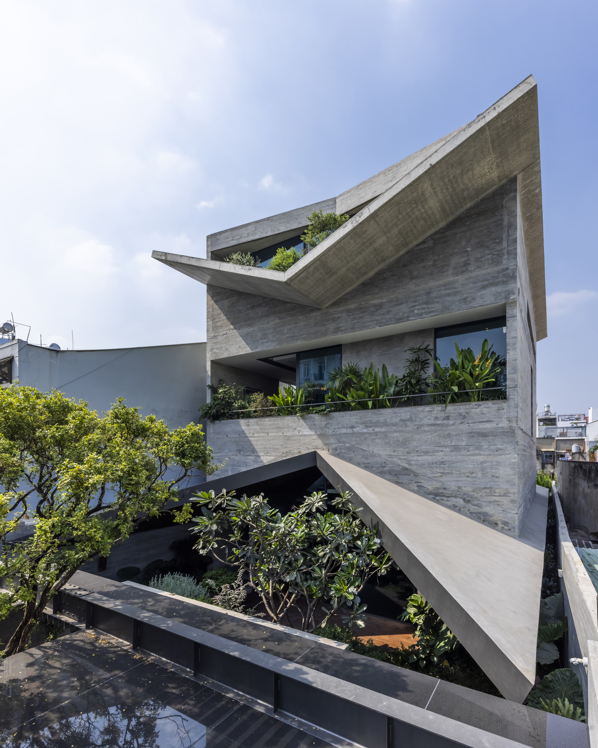Angled facade showing planted terraces with trees and cantilevered concrete slabs under scattered clouds