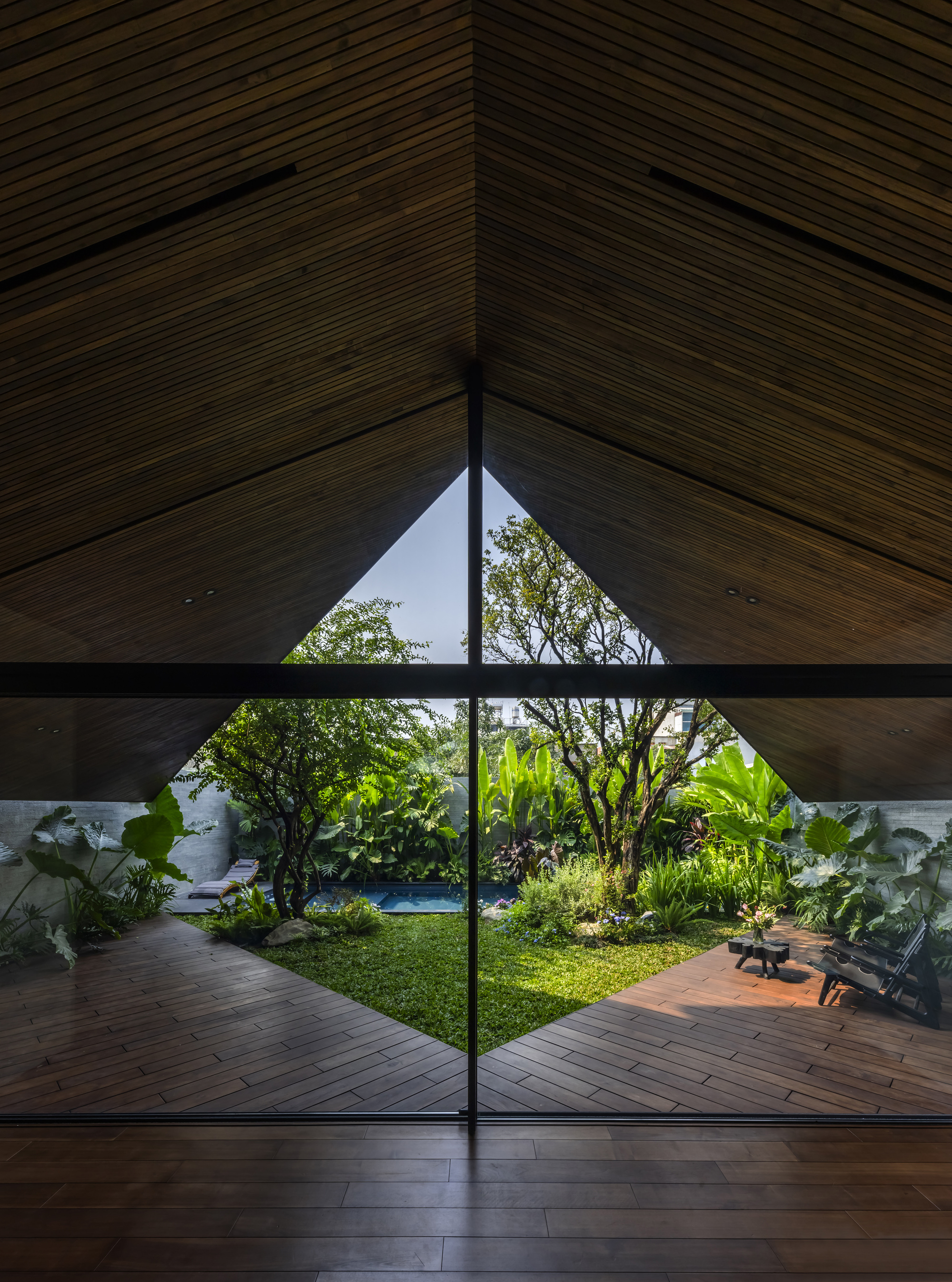 Triangular glazing framing a grass courtyard with lounge chairs and tropical planting at dusk