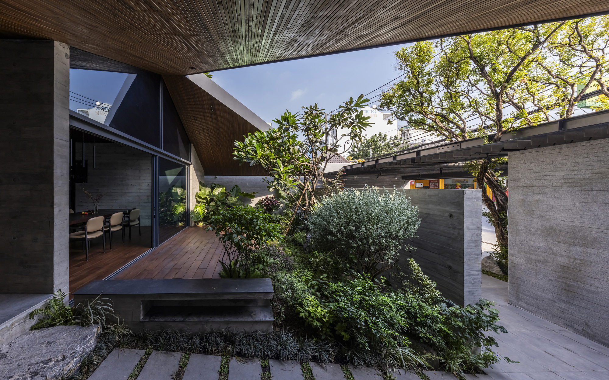 Courtyard deck with planted beds surrounded by board-formed concrete walls and mature trees overhead