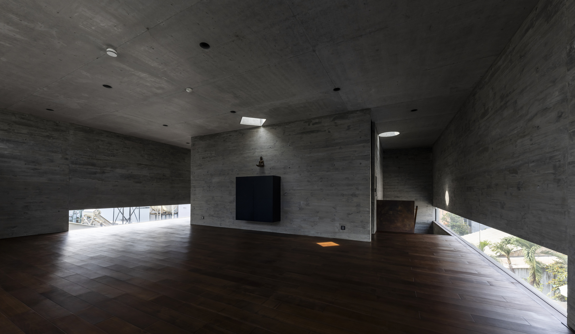 Double-height concrete interior space with dark timber flooring and horizontal strip windows