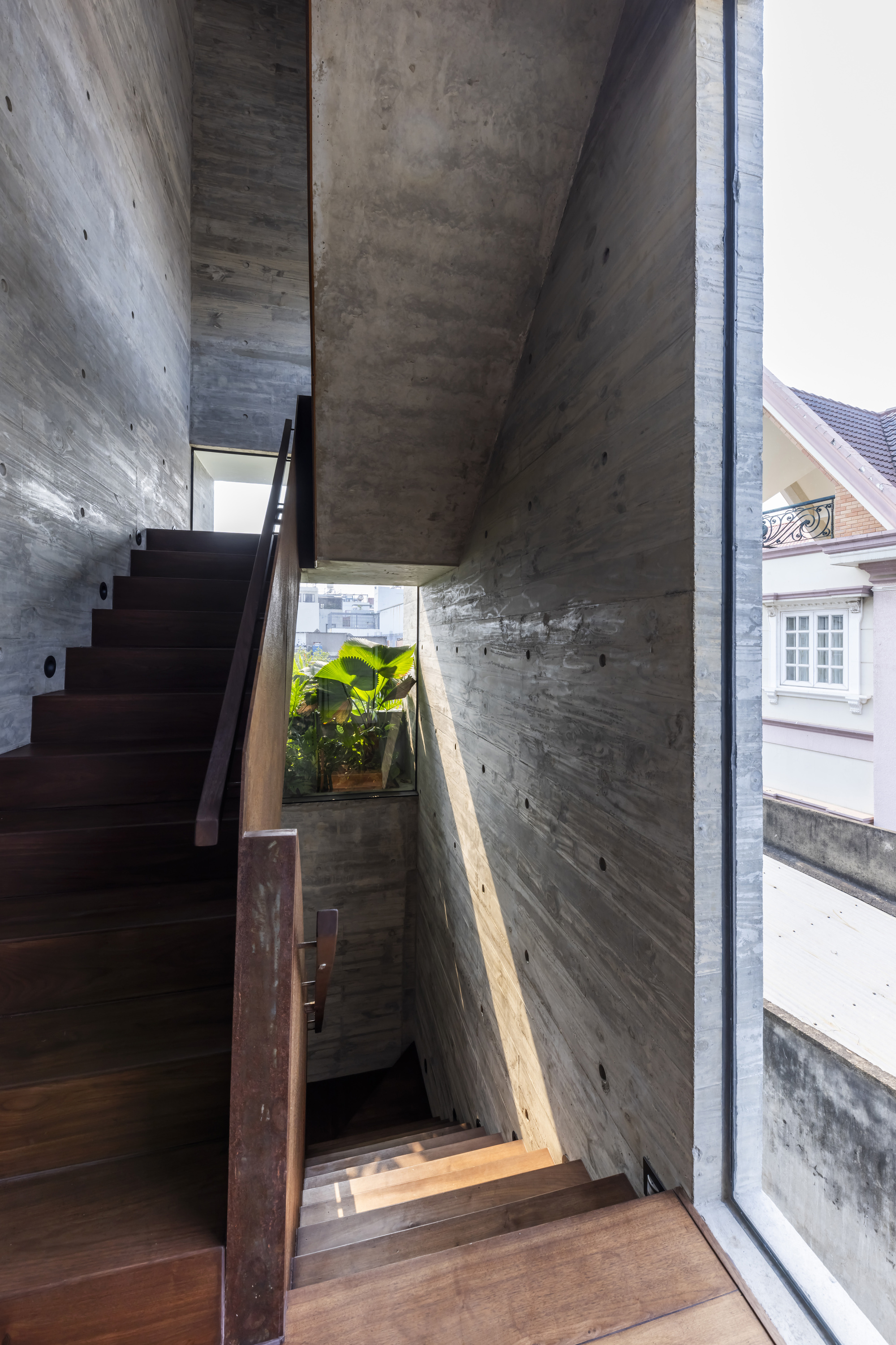 Multi-level concrete staircase with steel balustrade and narrow glazing overlooking neighboring buildings