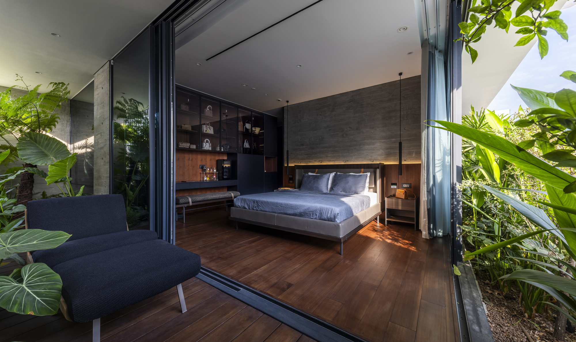 View through folding glass wall from planted terrace into bedroom with dark timber floors
