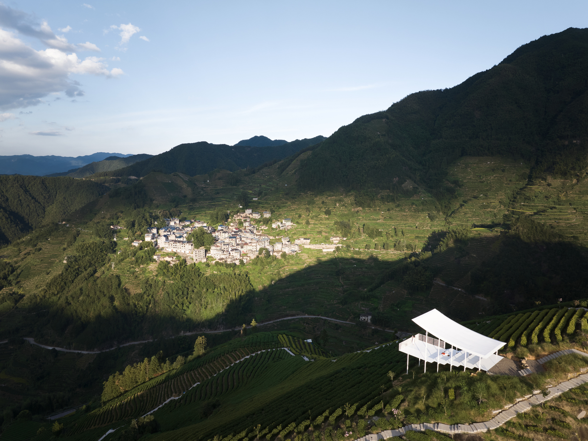 Aerial view of the white canopy structure on terraced hillside overlooking a valley settlement