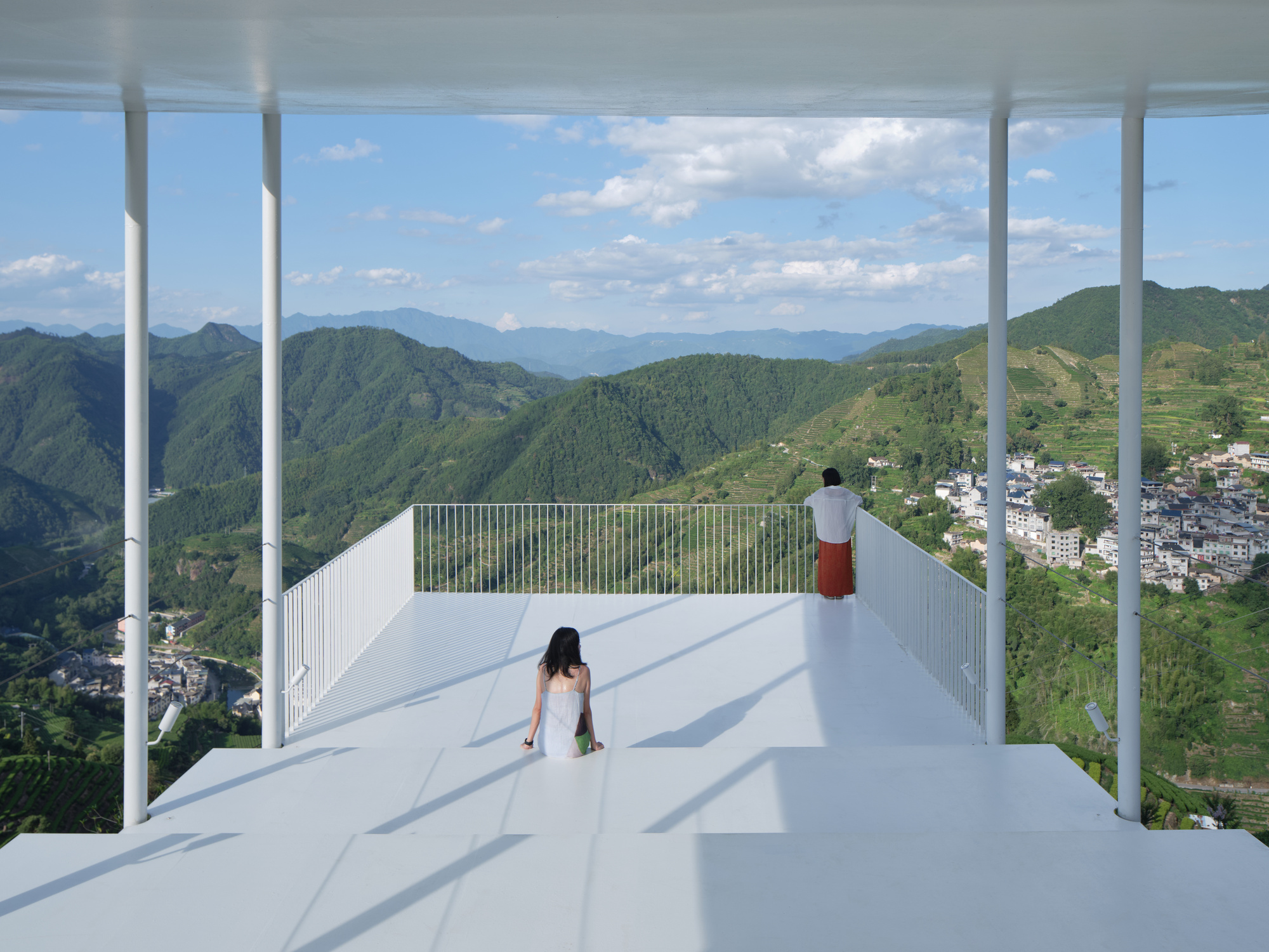 White metal roof deck with slender columns framing views of terraced fields and valley below