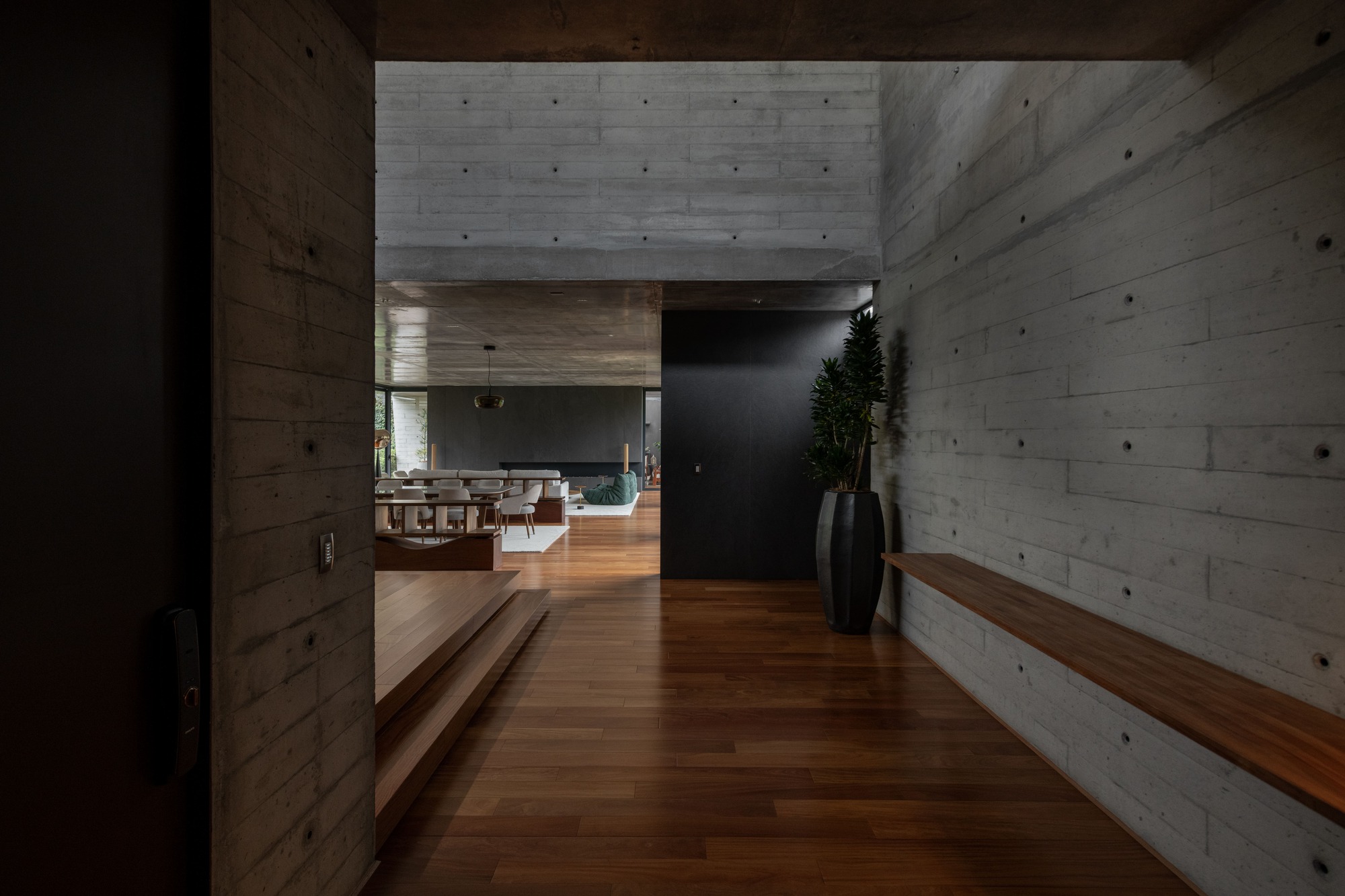 Hallway with board-formed concrete walls and timber flooring leading to a sunlit kitchen