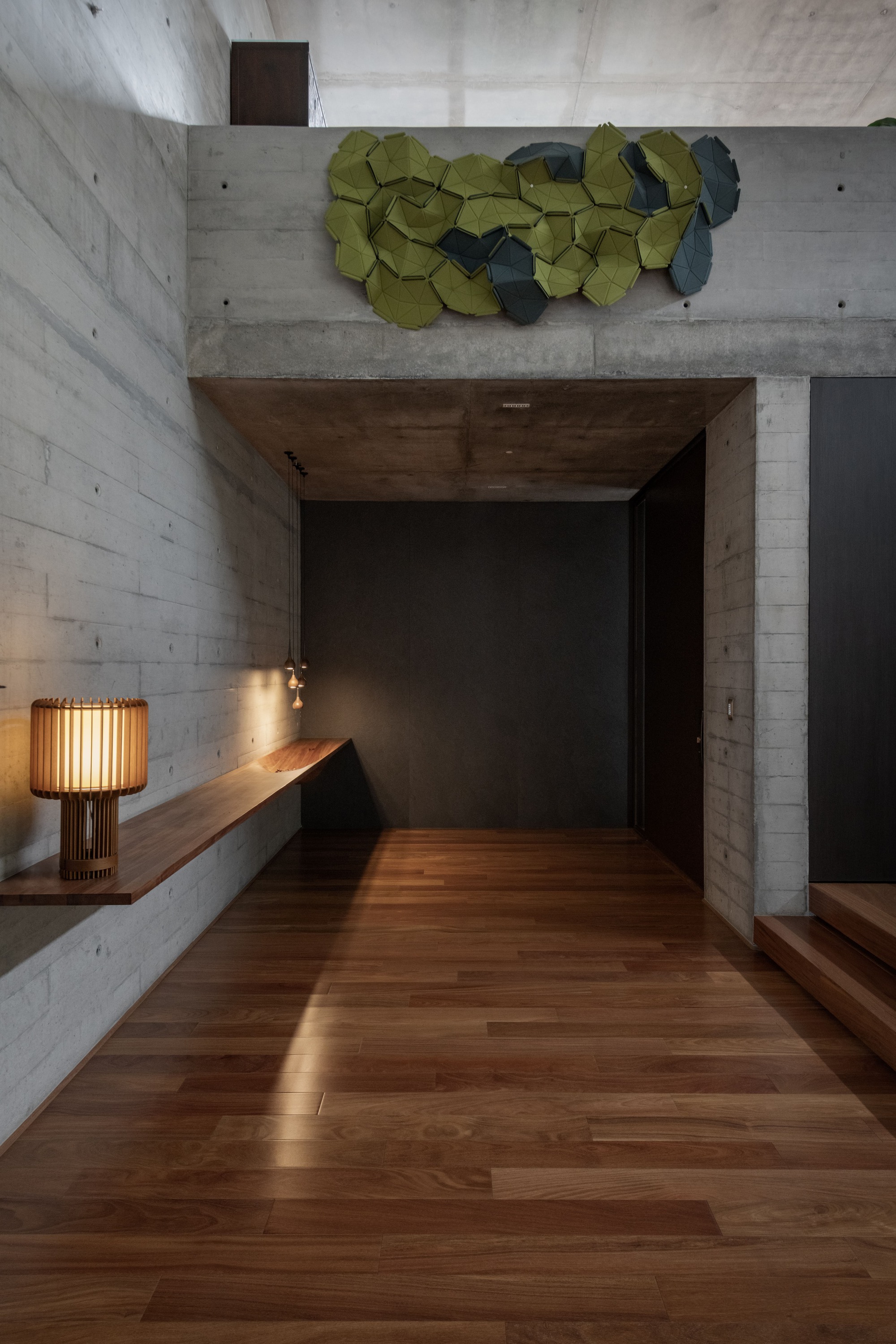 Corridor with concrete walls and timber flooring below a decorative wall sculpture
