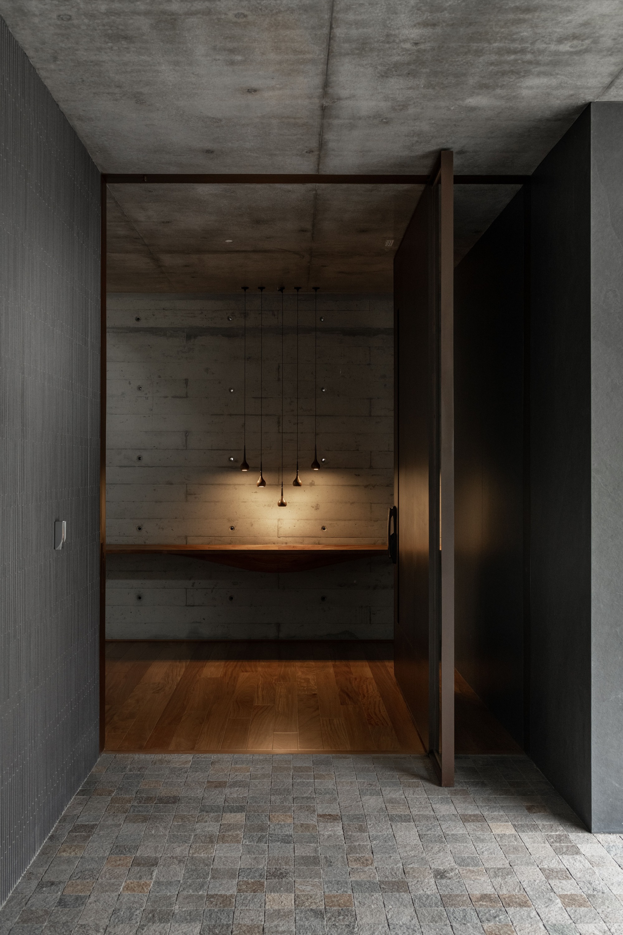 Entry threshold with brick pavers opening to a board-formed concrete alcove with pendant lights