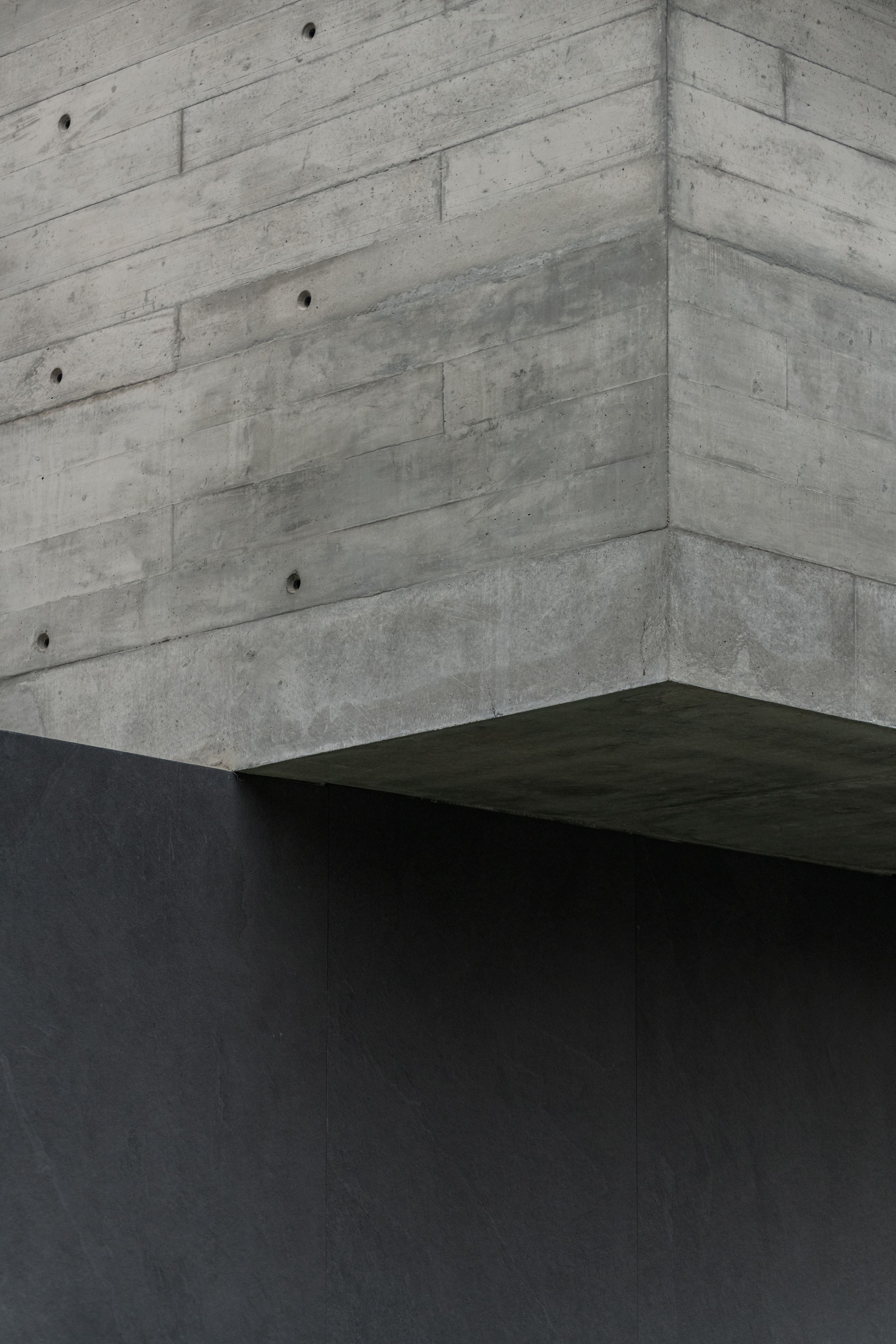 Corner detail of board-formed concrete walls meeting a dark cantilevered volume
