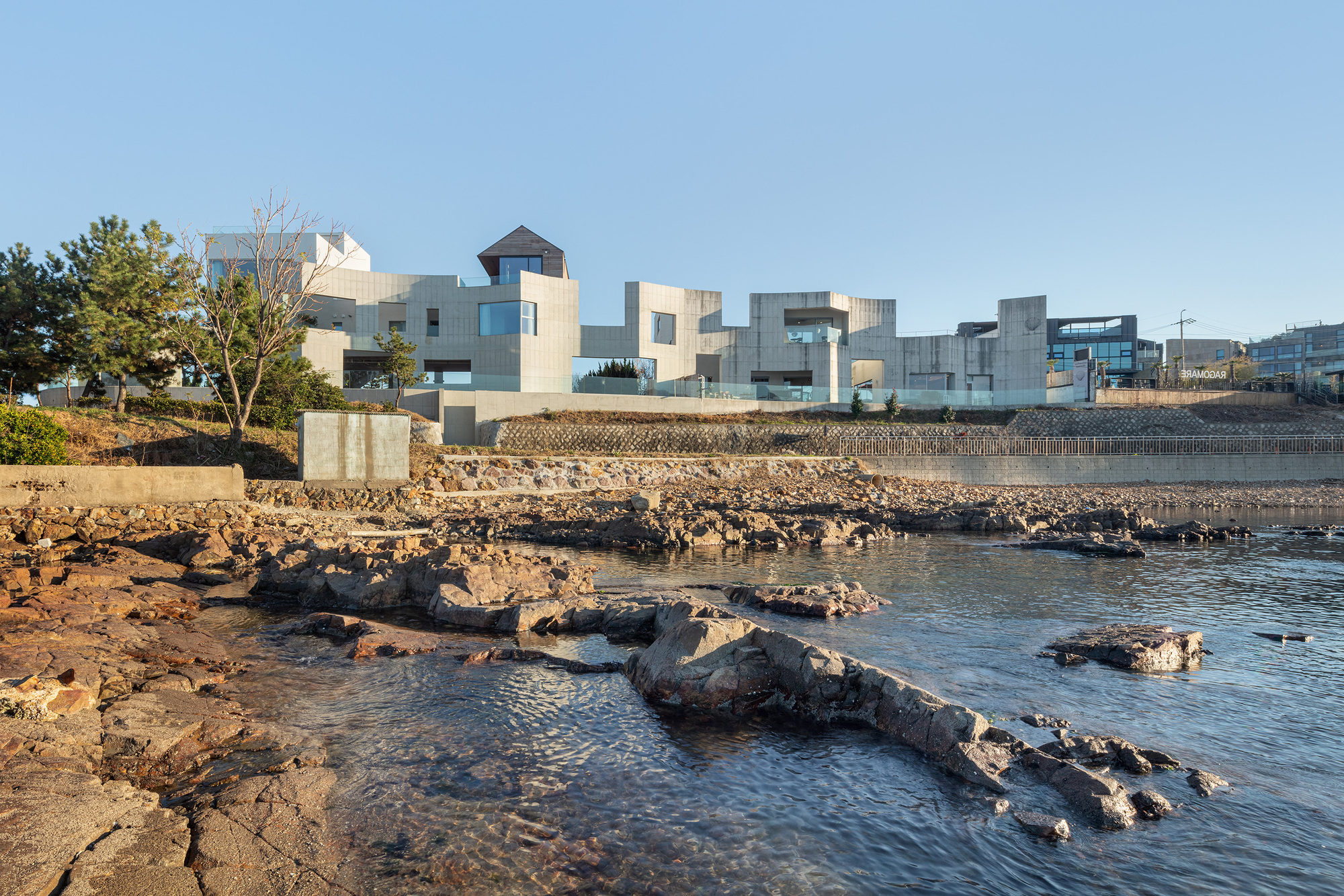 Coastal view of the white stucco volumes rising above volcanic rock outcrops at low tide