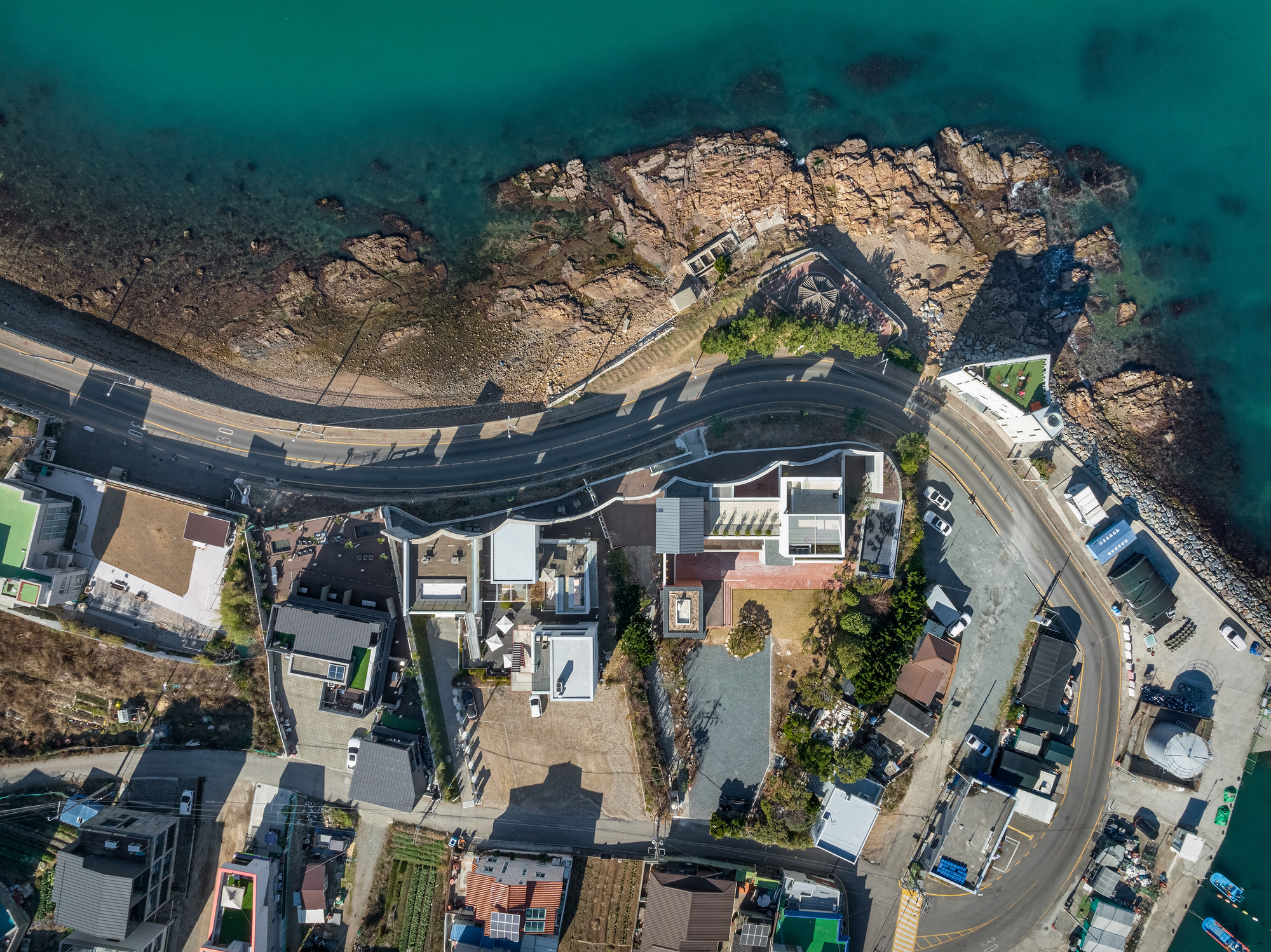 Overhead drone view showing the coastal road curving between the residences and rocky waterfront
