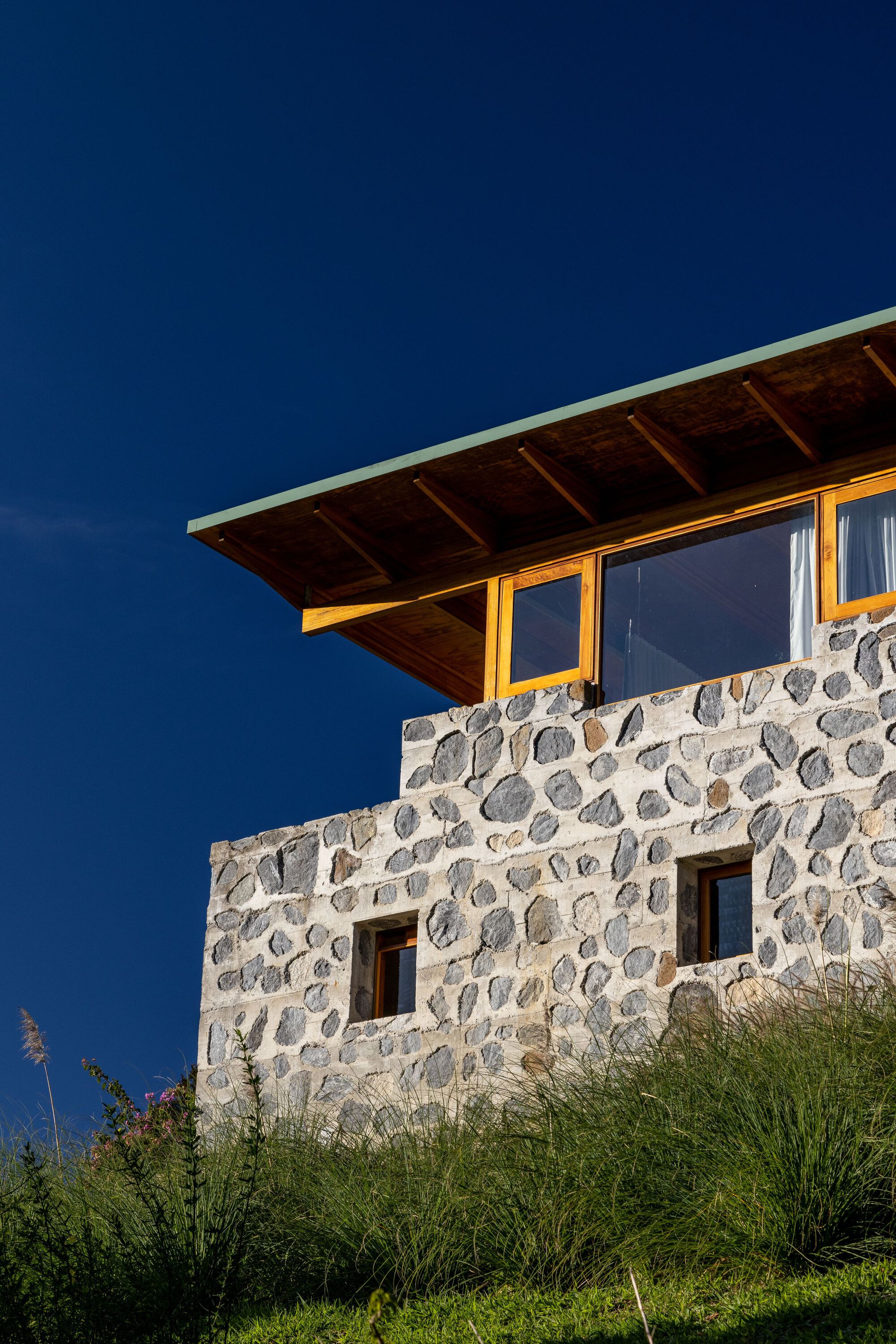 Upper level facade with river stone walls and timber roof overhang against deepening twilight sky