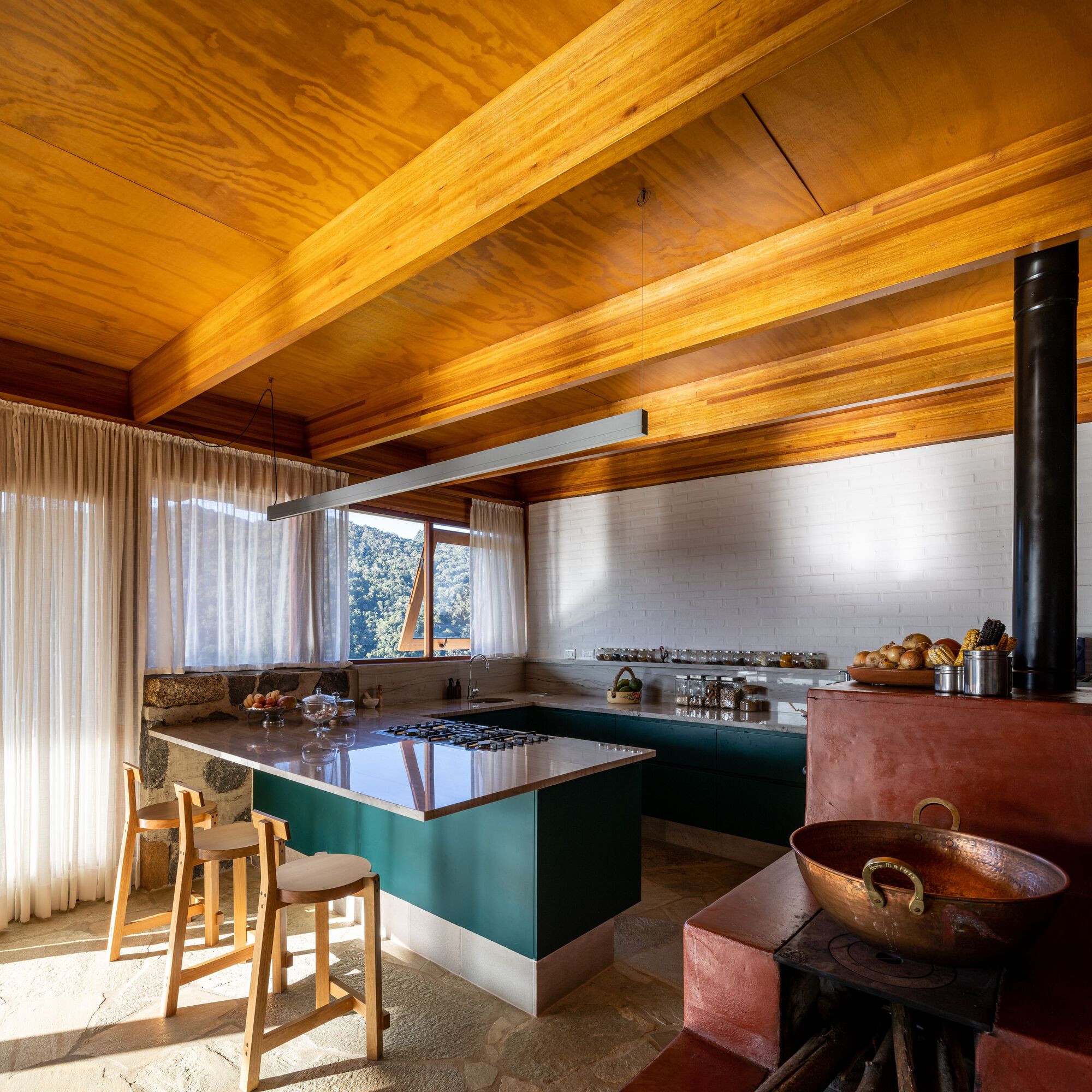 Kitchen with green island and wood-burning stove beneath exposed timber beams and a slatted wood ceiling
