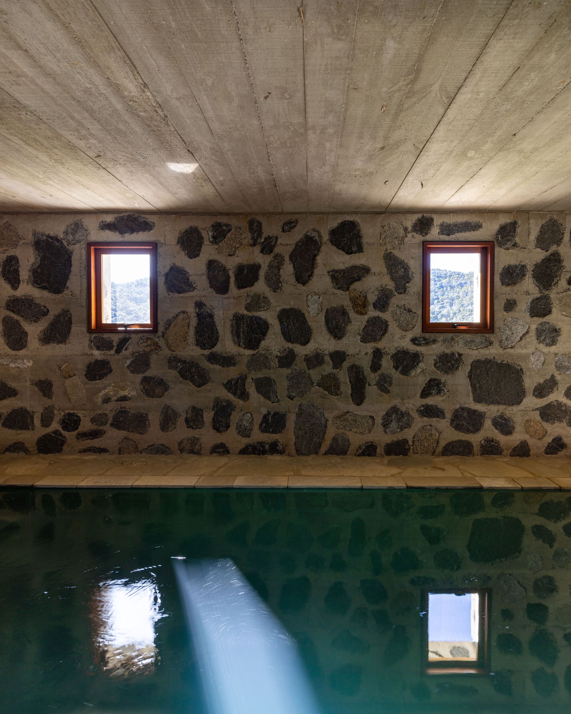 Indoor pool with fieldstone walls and board-formed concrete ceiling reflecting natural light from framed windows