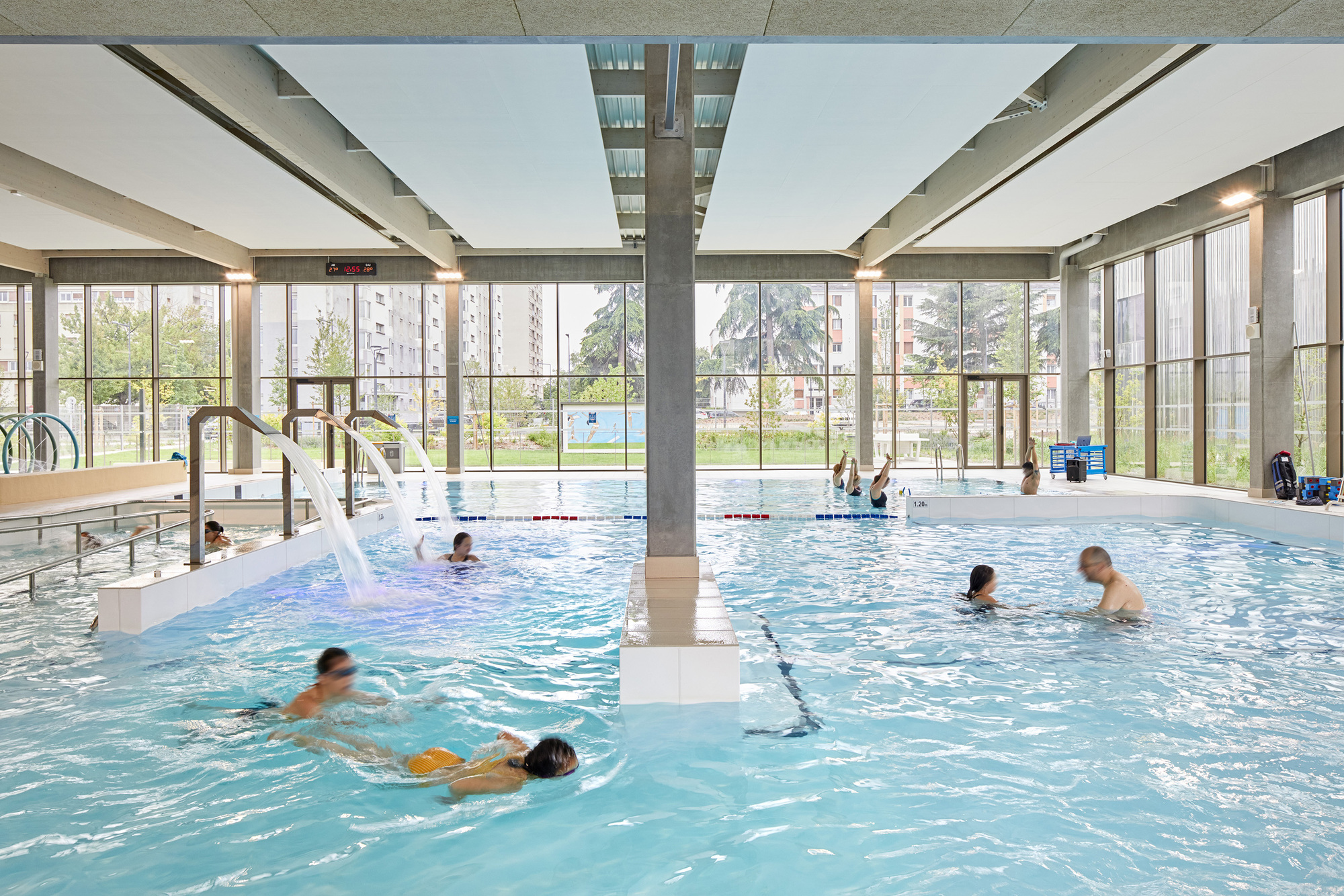 View across the pool to floor-to-ceiling glazing and a sunlit park beyond the water