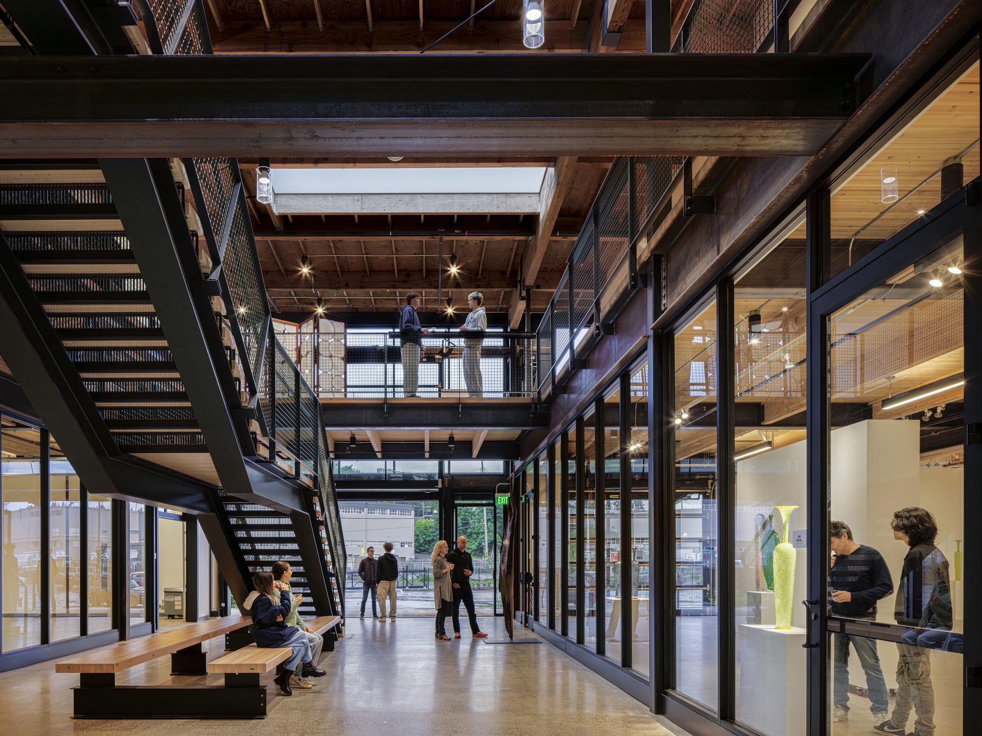 Three-story interior atrium with steel mesh stairs, timber ceiling joists, and glass-walled offices