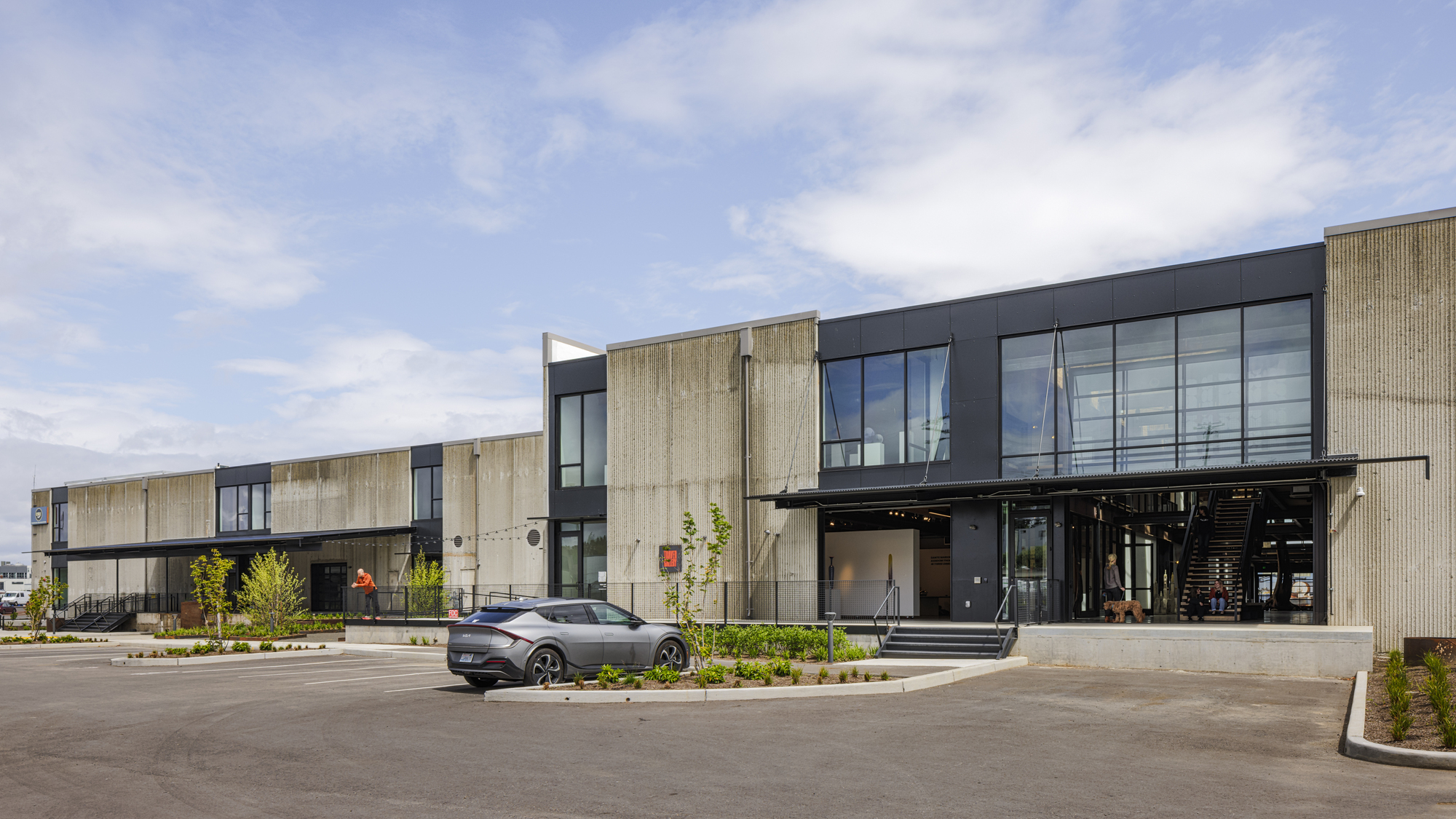 Street view of the two-storey facade combining light timber cladding and dark metal panels with a canopied entry