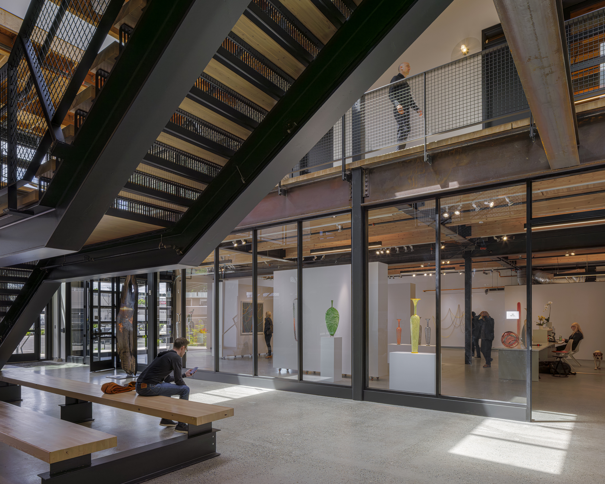 Open stairwell with metal mesh balustrades and glazed gallery wall displaying ceramic sculptures under natural daylight