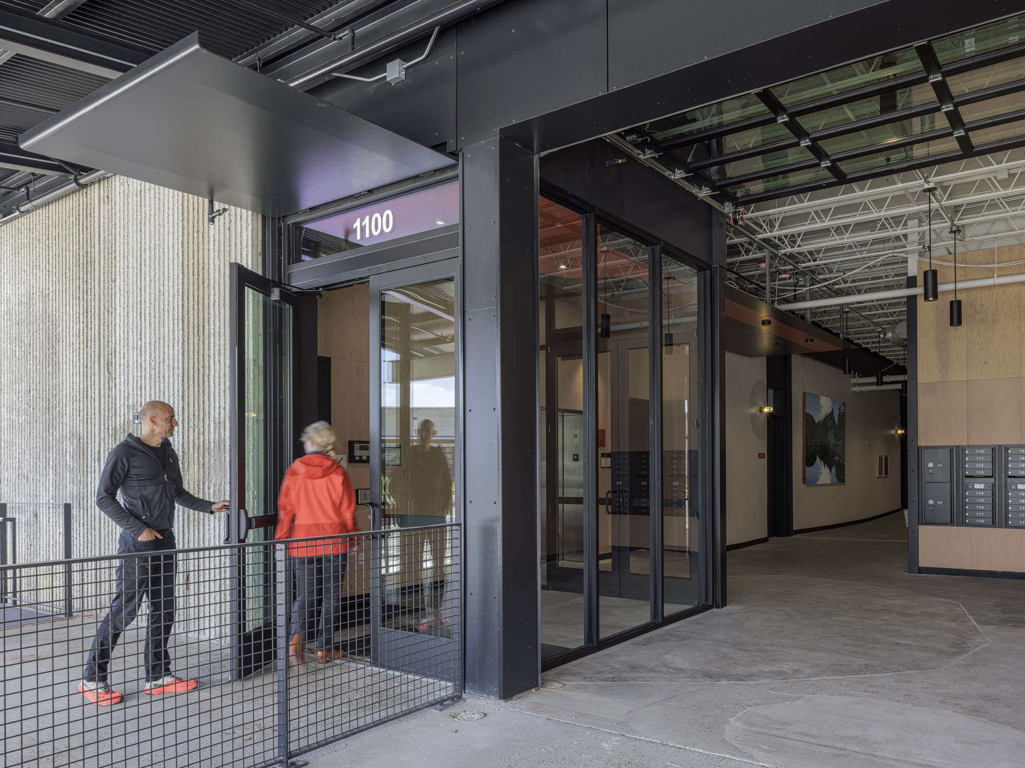 Mezzanine landing with metal mesh railings and glazed doors leading to numbered tenant spaces under exposed services