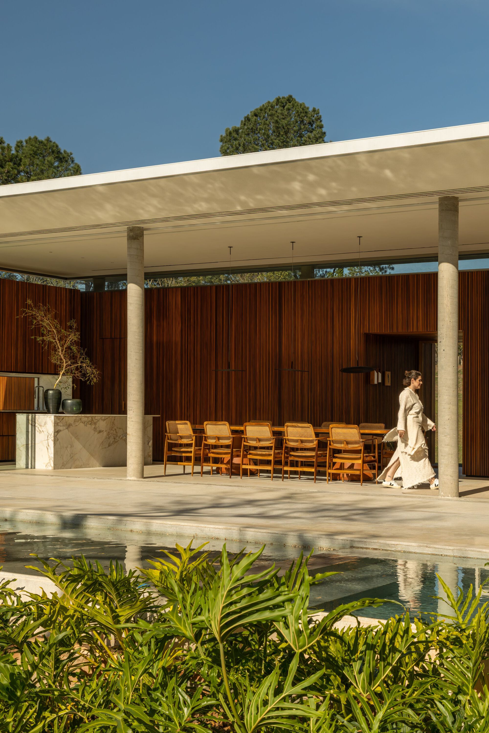 Covered terrace with marble planter, leather lounge chairs and a figure walking beside the pool