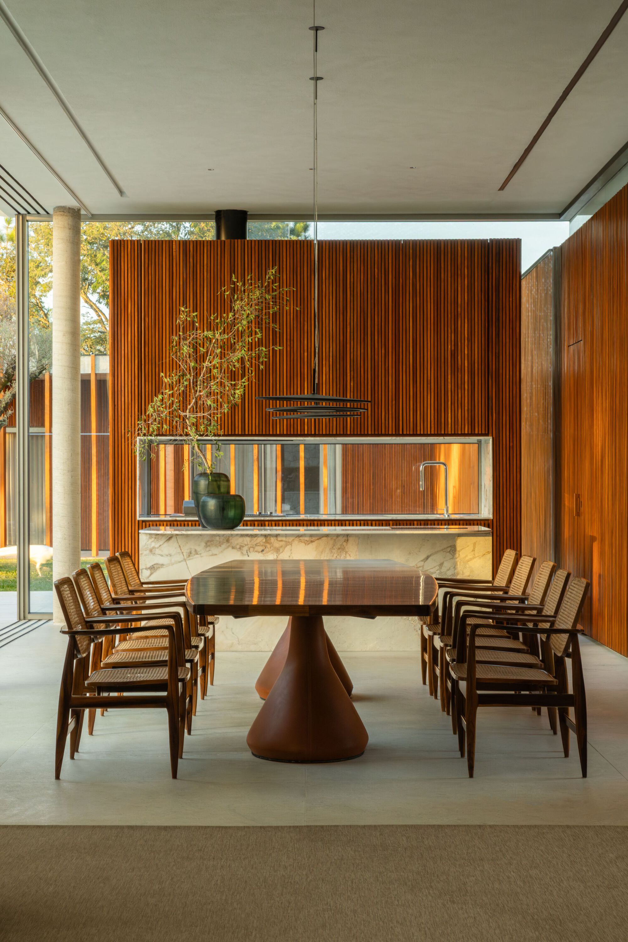 Dining room with sculptural timber table beneath vertical wood slat walls and clerestory windows