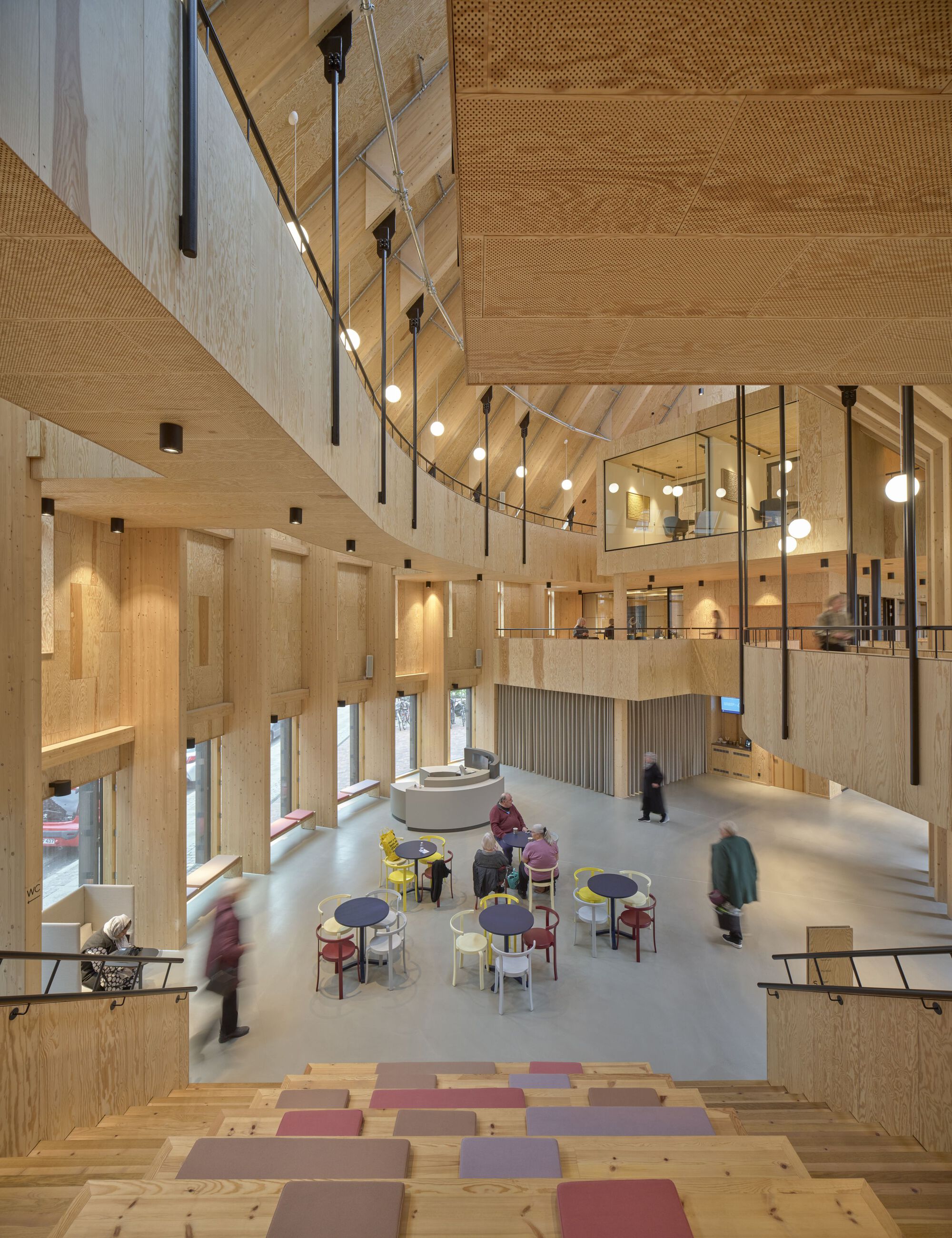 Multi-level interior atrium with timber walls, suspended globe lights, and visitors seated below