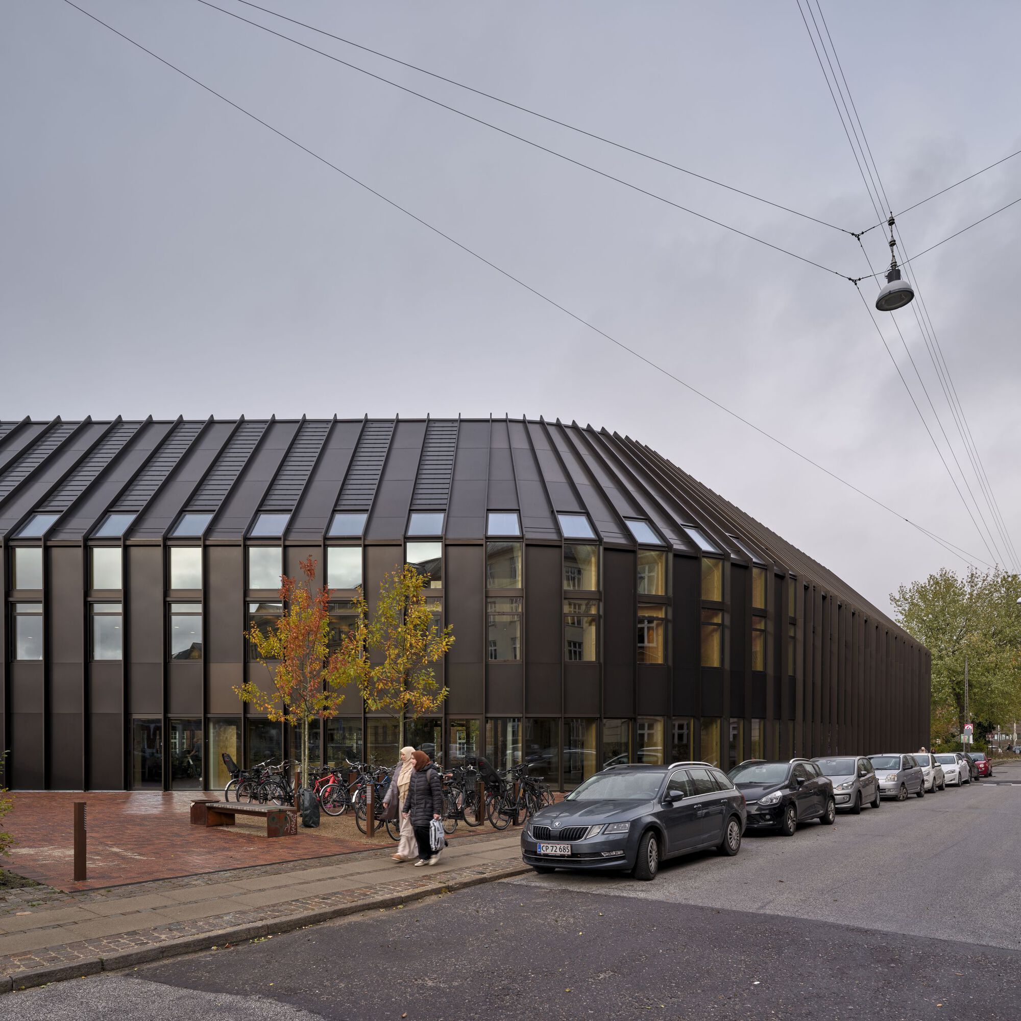 Street view of ribbed metal roof and facade with parked bicycles under autumn trees