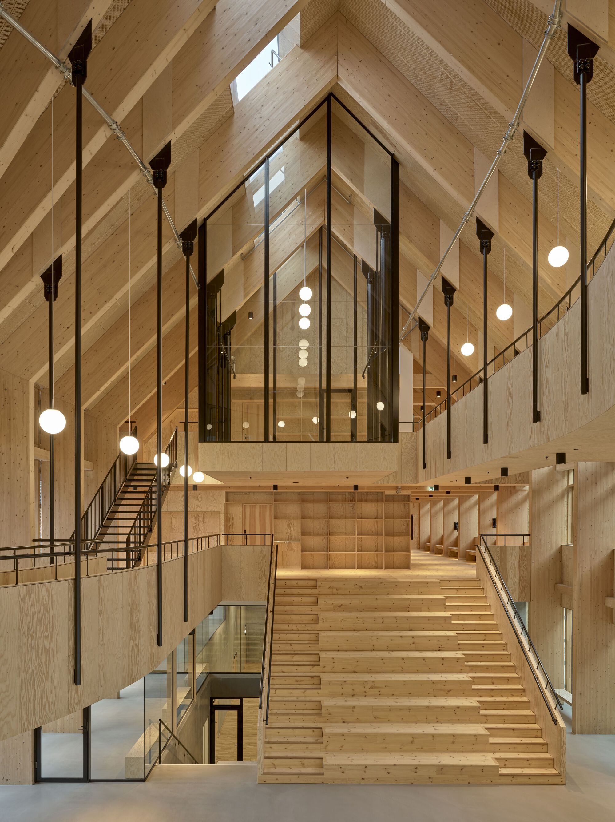 View up the stepped timber seating amphitheatre beneath diagonal laminated wood beams and pendant lighting