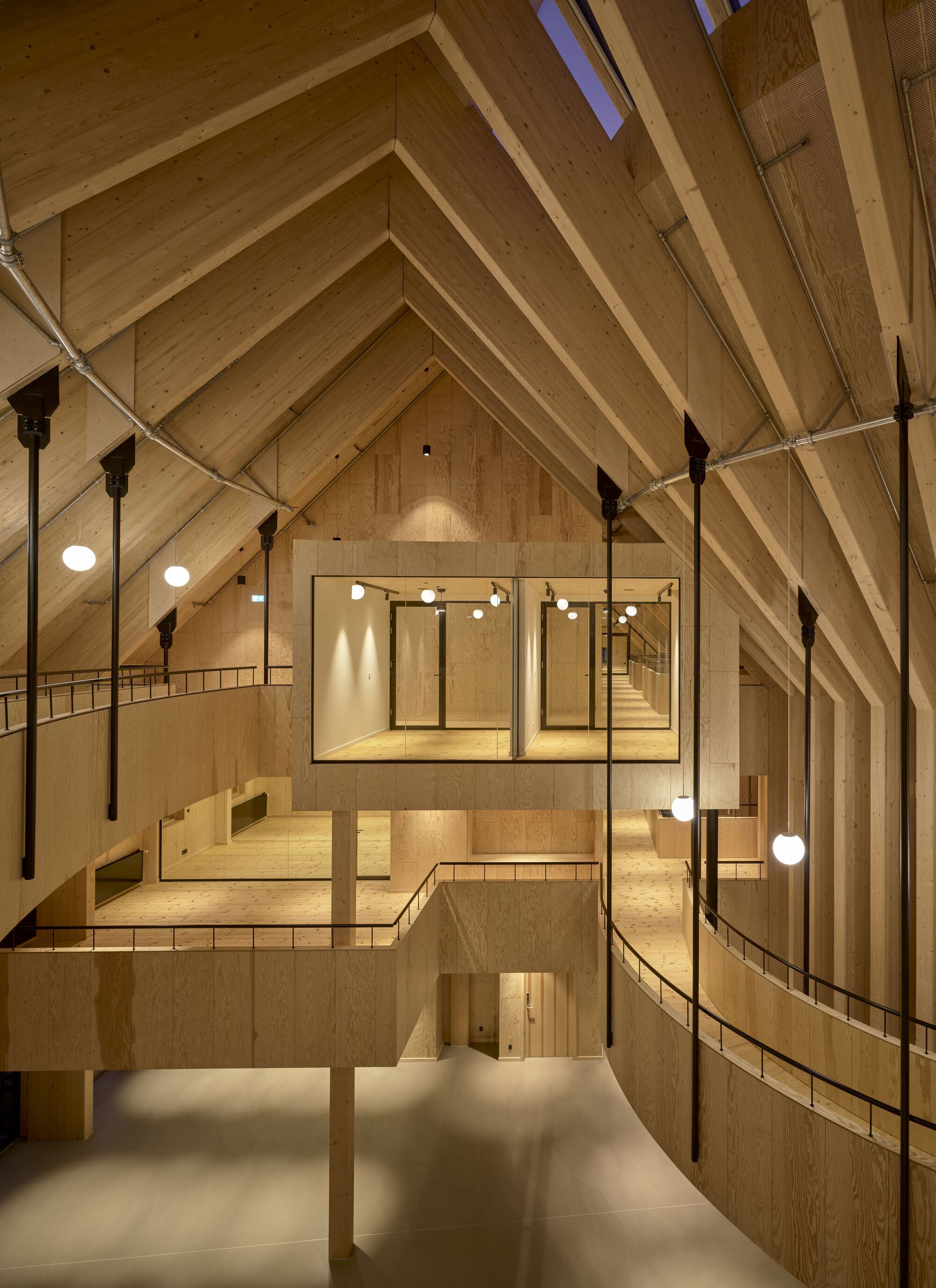 Interior view of the timber-clad volume showing exposed rafters, layered mezzanines and suspended globe pendants