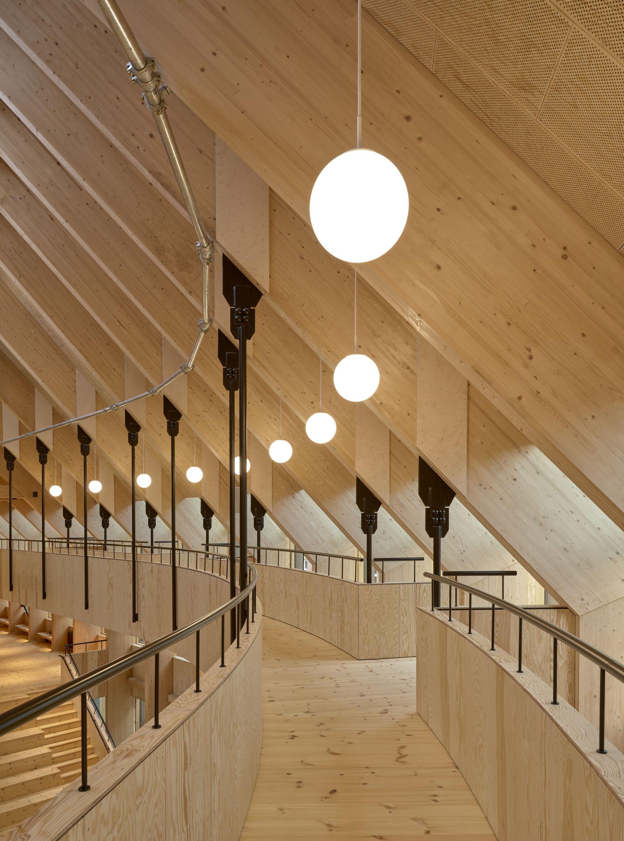 Narrow walkway along the upper gallery with cable railings and pendant lights beneath the angled timber ceiling