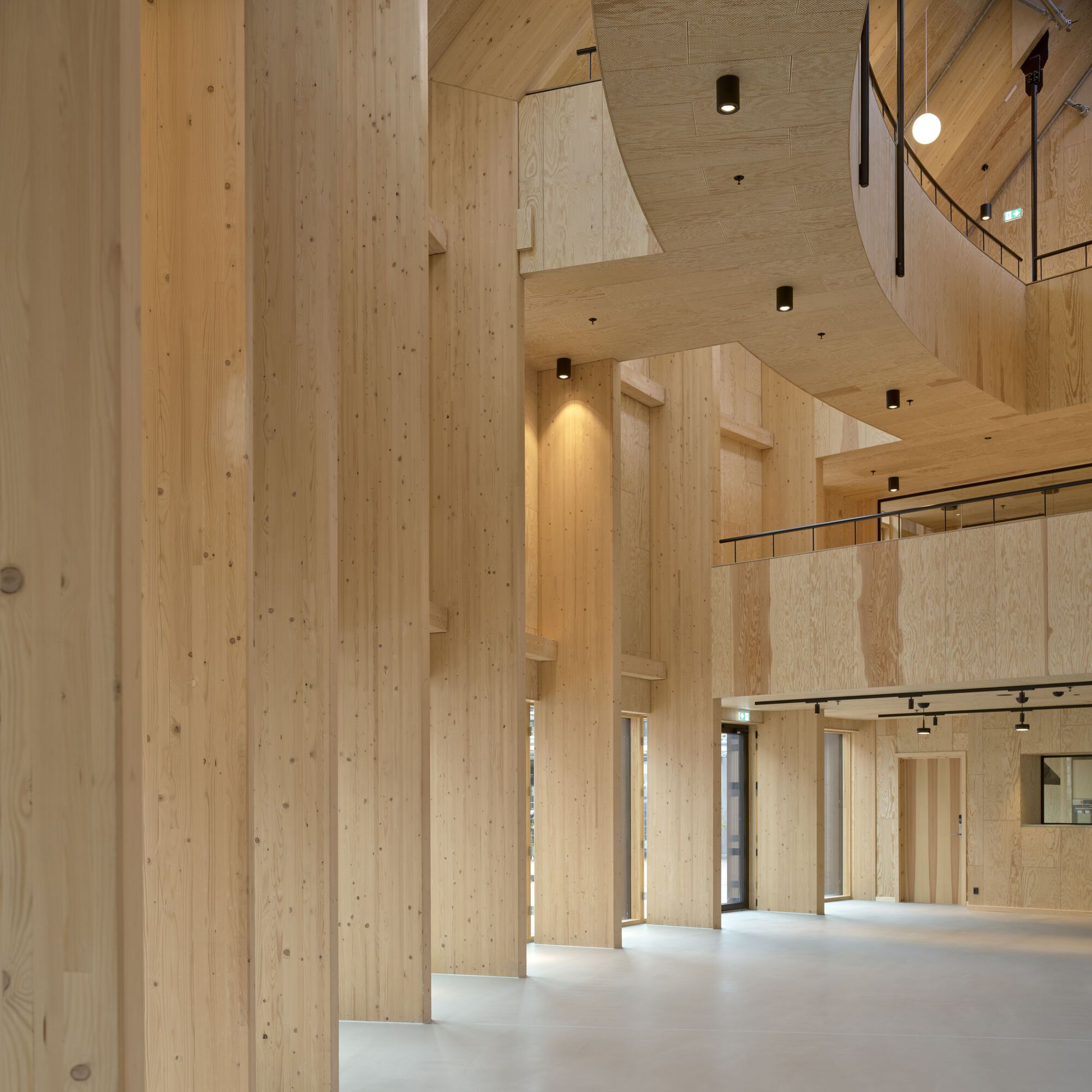 Double-height interior space showing laminated timber columns, exposed beams and mezzanine balustrade with glass railing