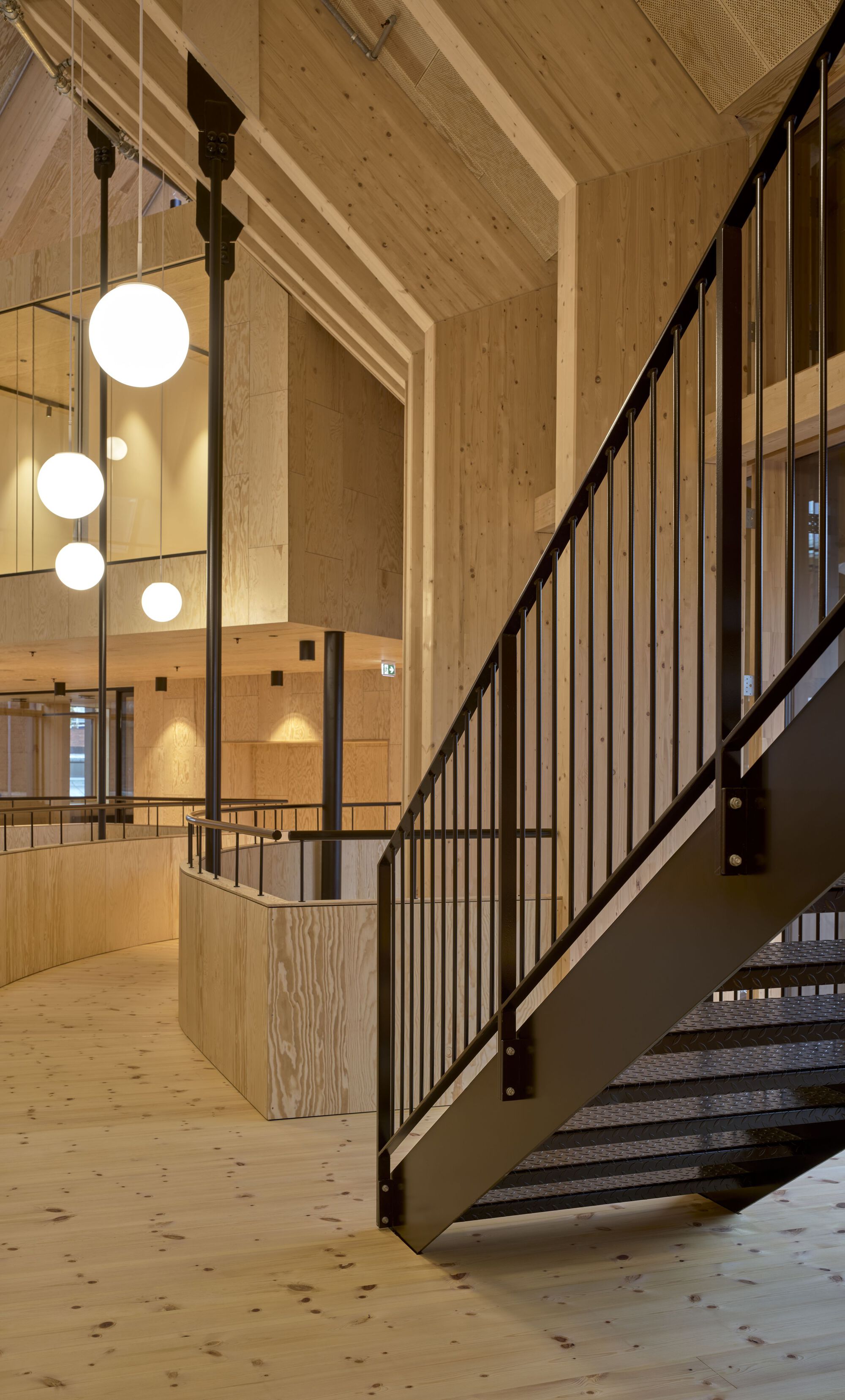 Metal staircase with vertical balusters and globe pendant lights in a timber-lined atrium
