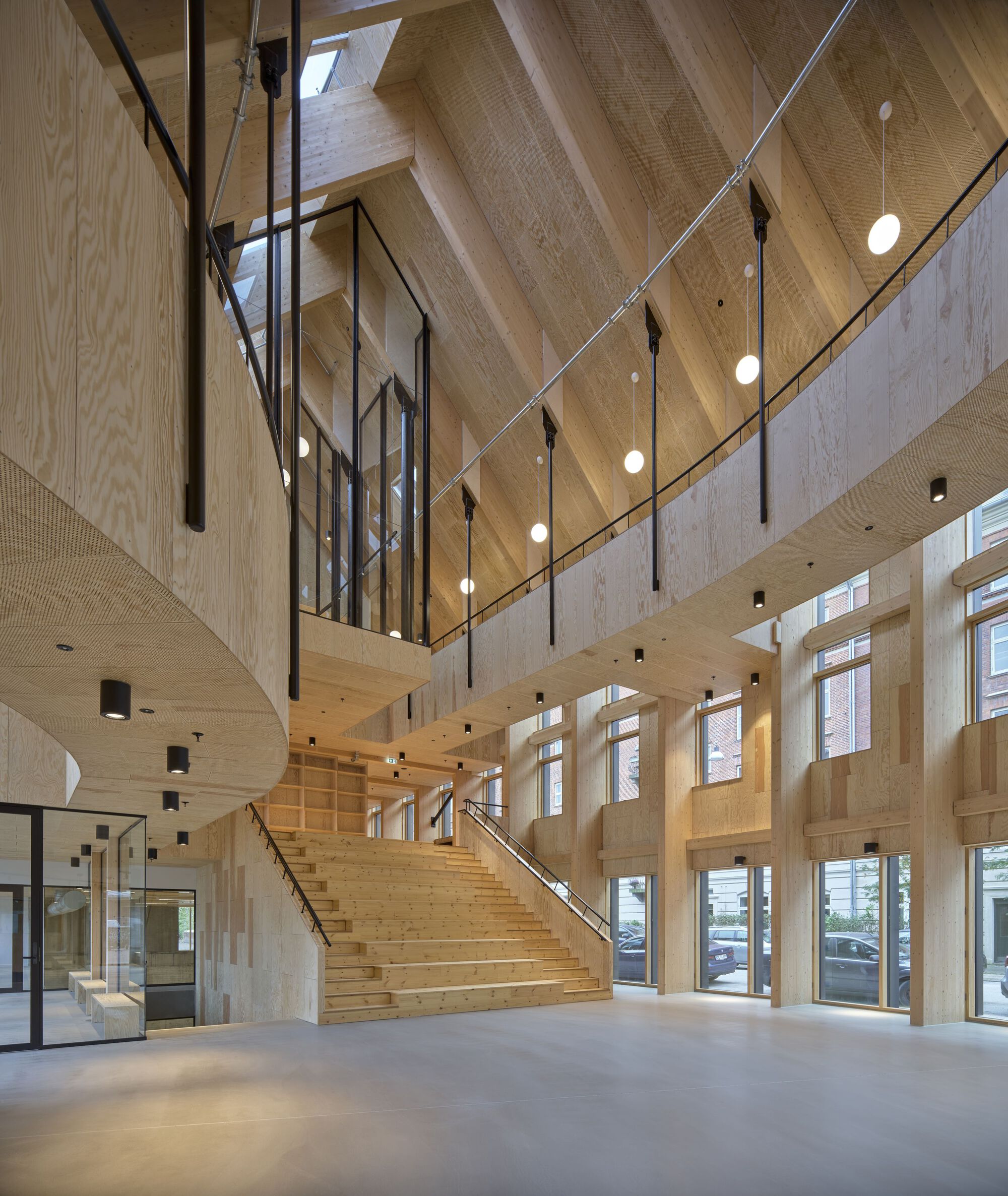 Entrance foyer with wide timber staircase rising toward vaulted wood ceiling and tall glazed facades