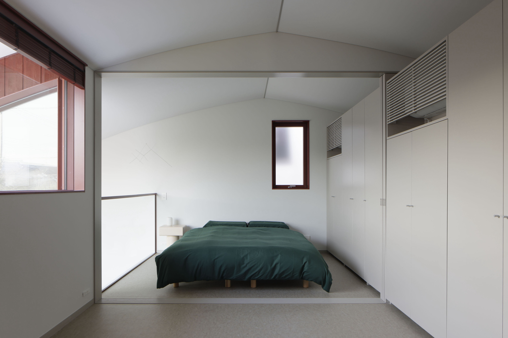 Bedroom with vaulted ceiling, built-in wardrobes and narrow vertical window framing distant view