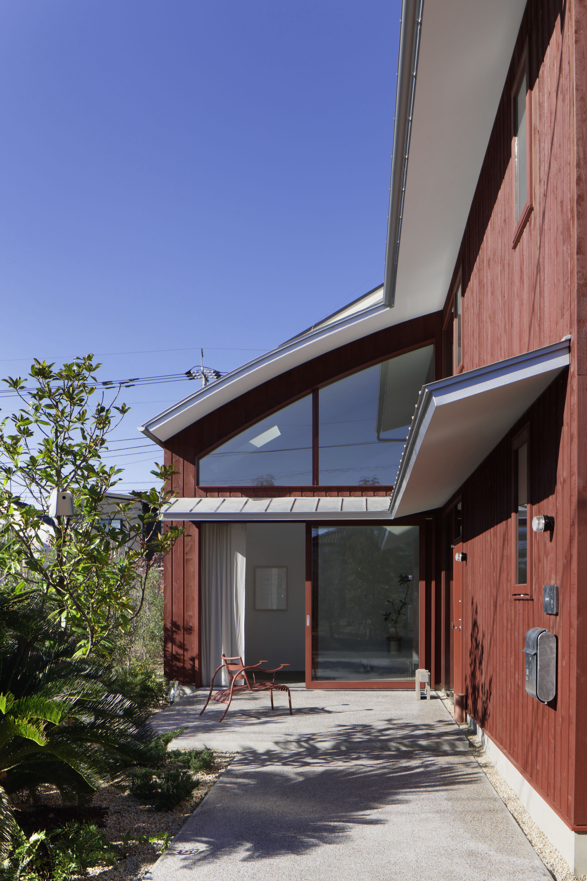Entry porch with curved glazed roof and concrete path casting shadows under clear sky