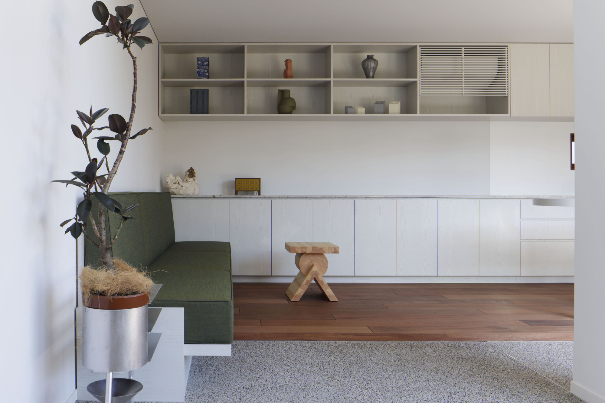 Built-in bench with green upholstery beside timber step-up platform and wall-mounted shelving unit