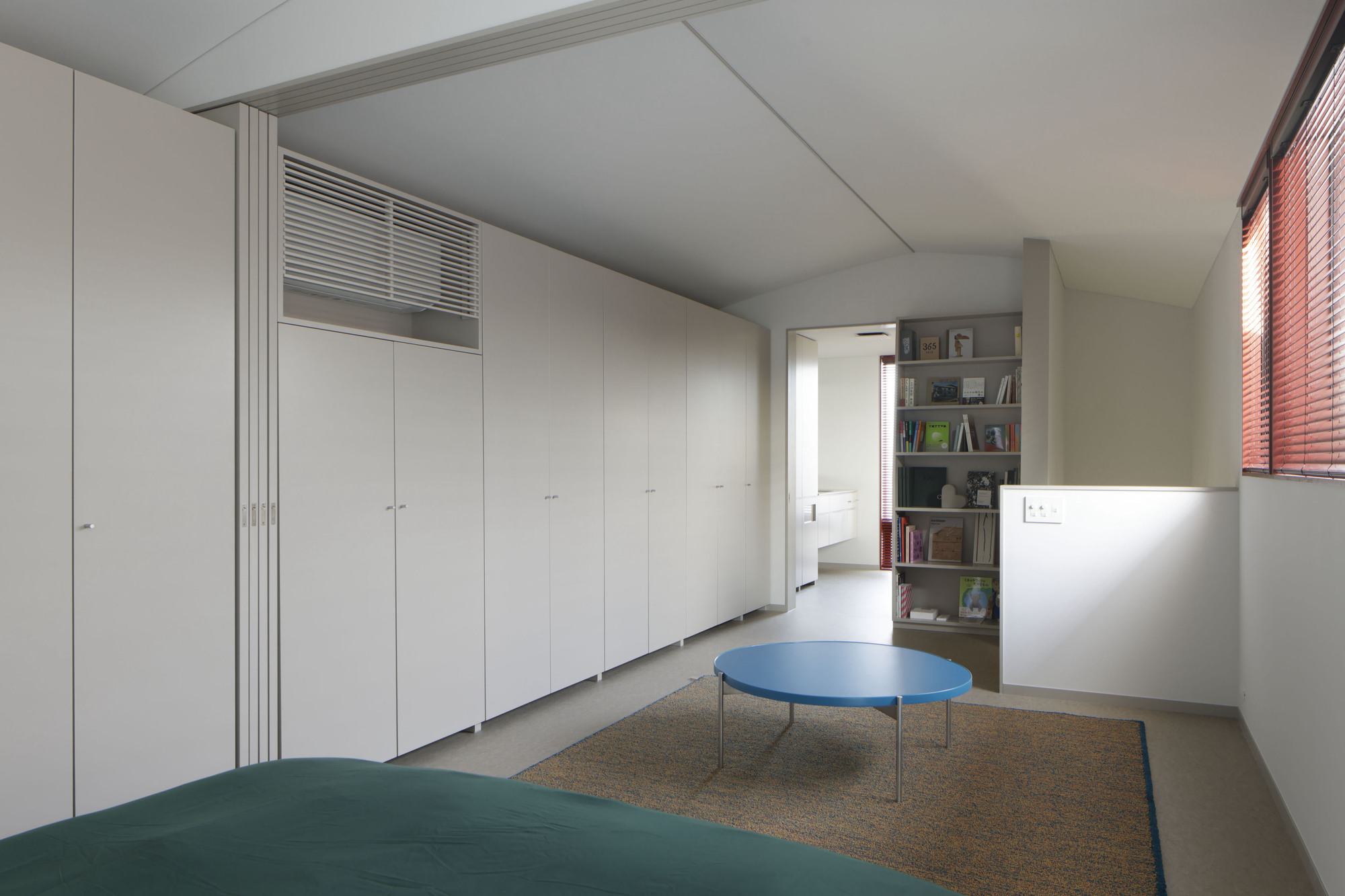 Bedroom with wall of white closets and terrazzo flooring under venetian-blinded window
