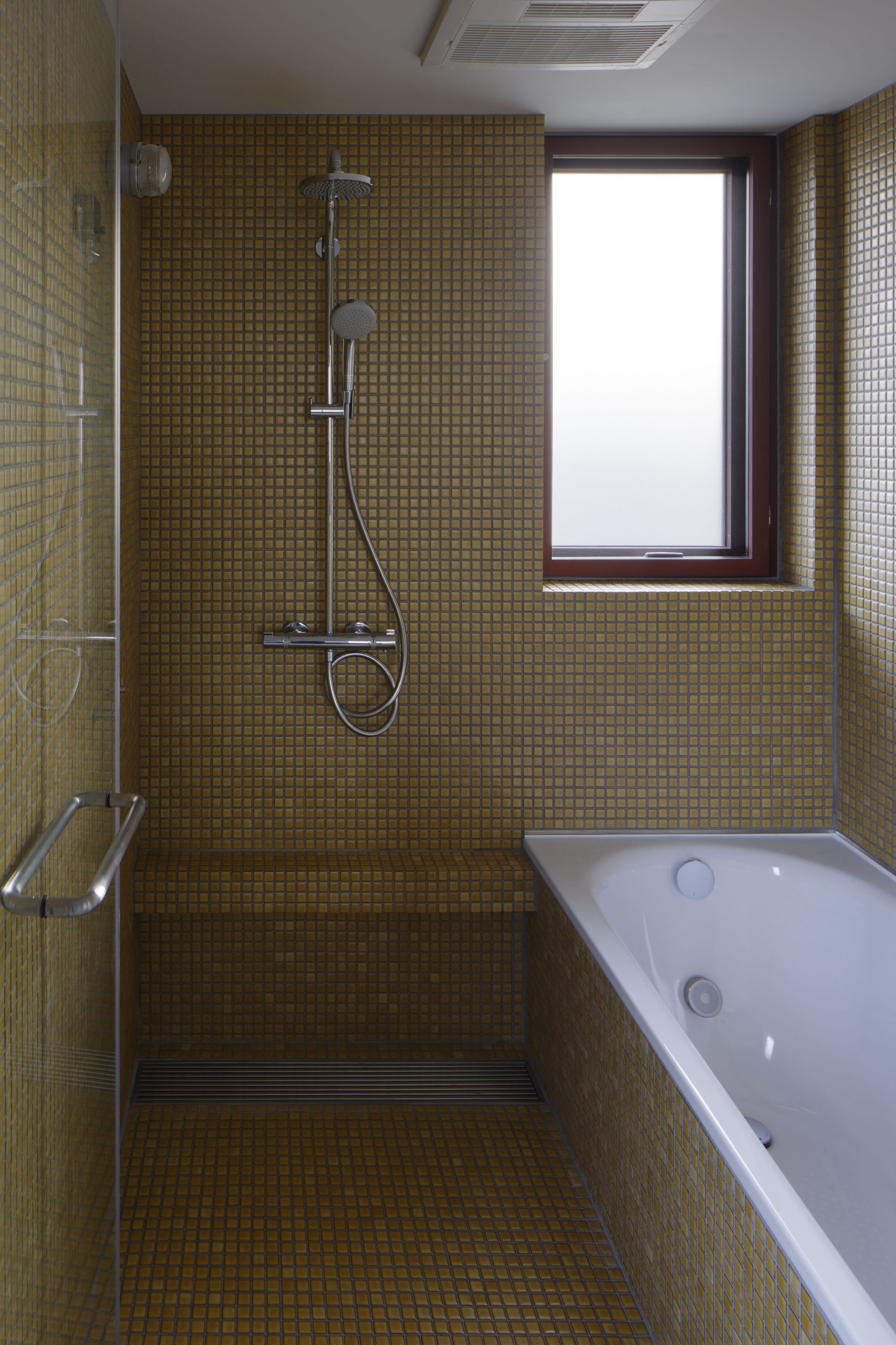 Bathroom interior with golden mosaic tile walls, walk-in shower, white bathtub and frosted window