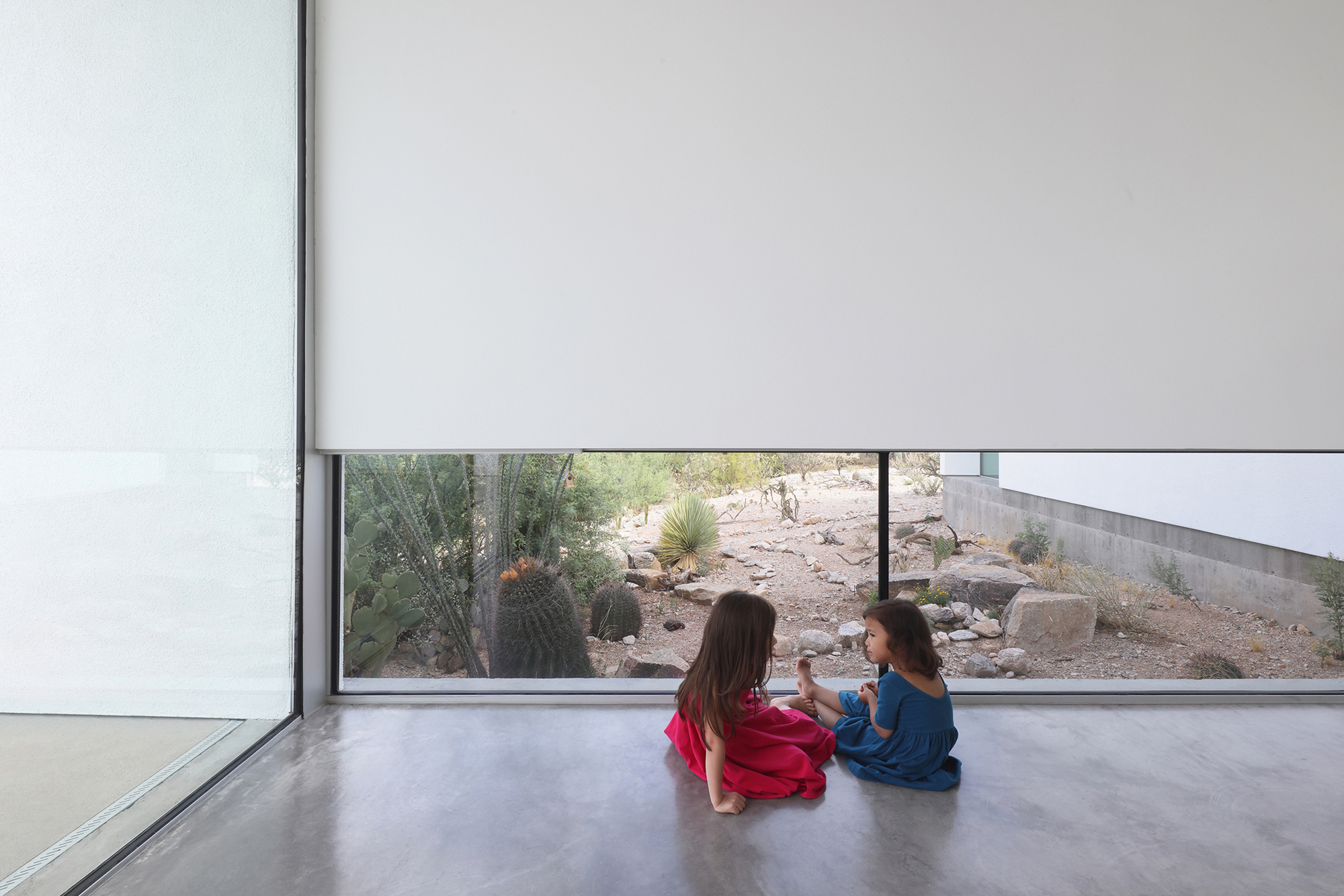 Low horizontal window framing desert landscaping with two children seated on polished concrete floor