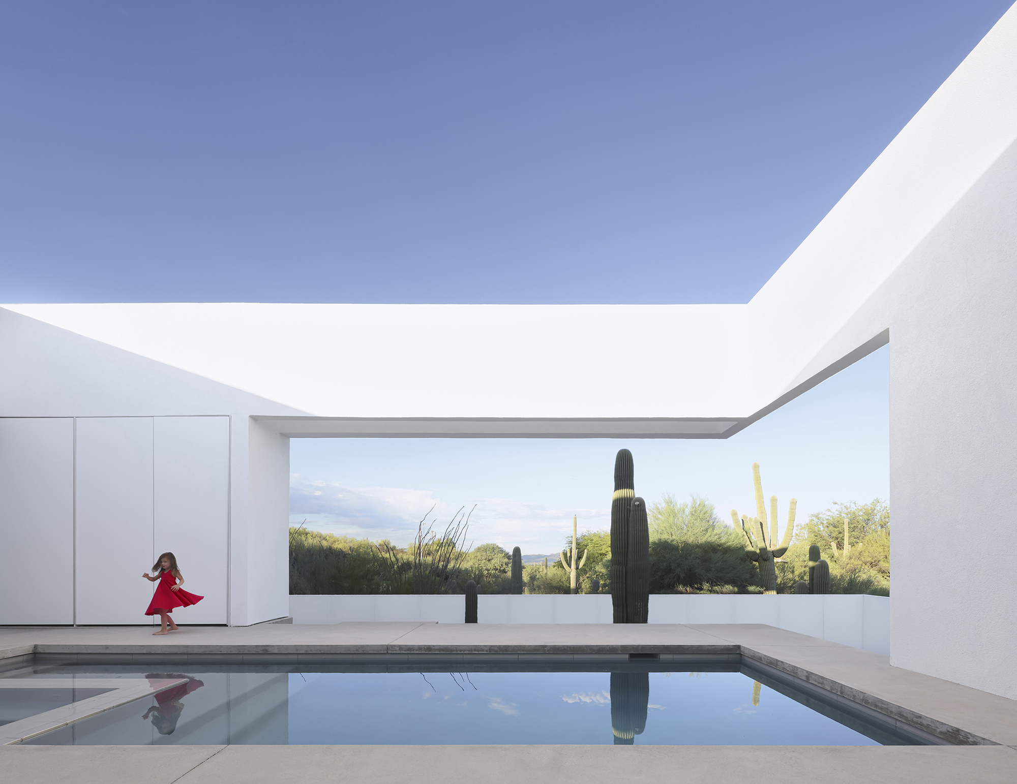 Courtyard pool reflecting white walls and sky with a child running across the deck