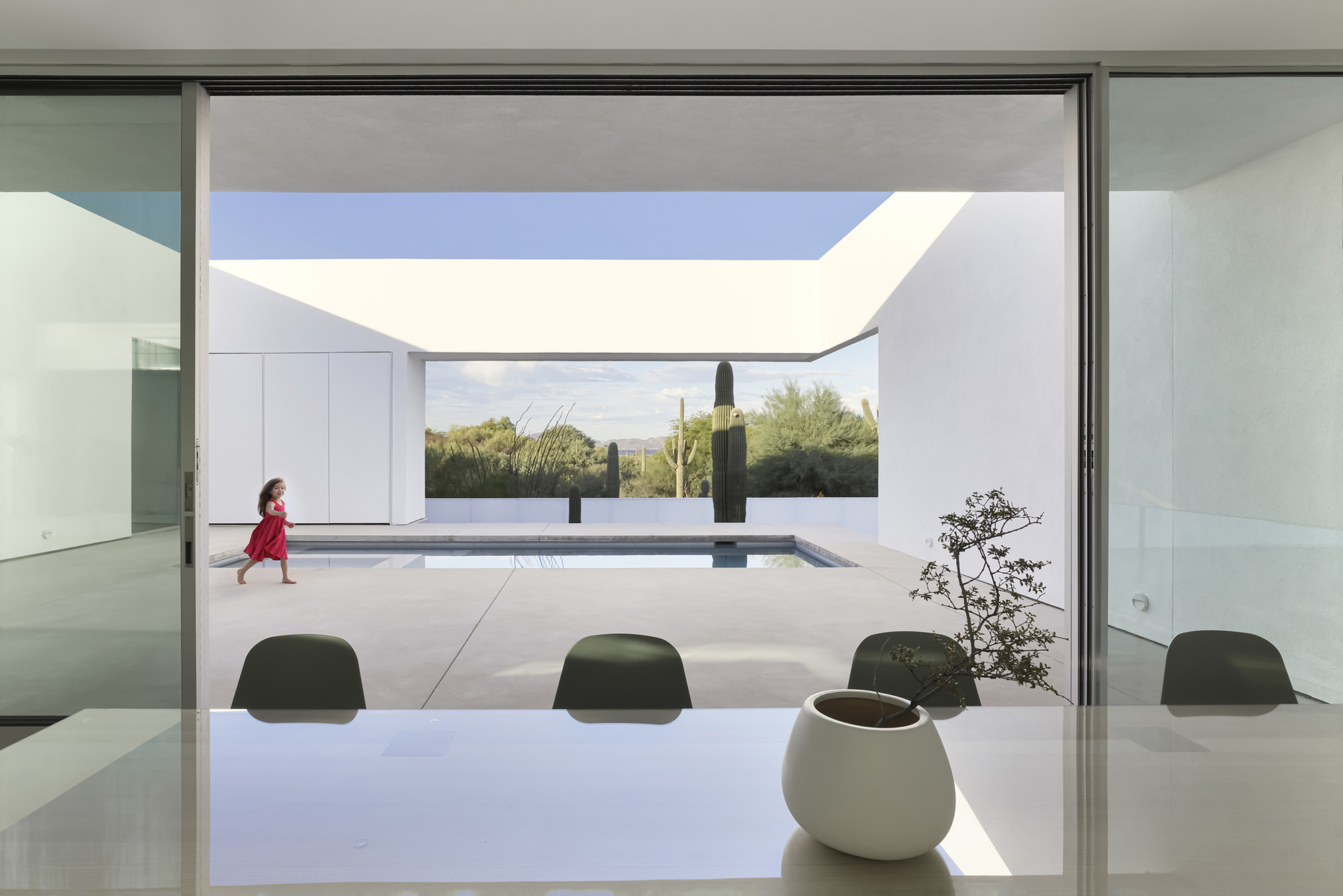 Interior view through dining table toward framed courtyard with pool and child walking past