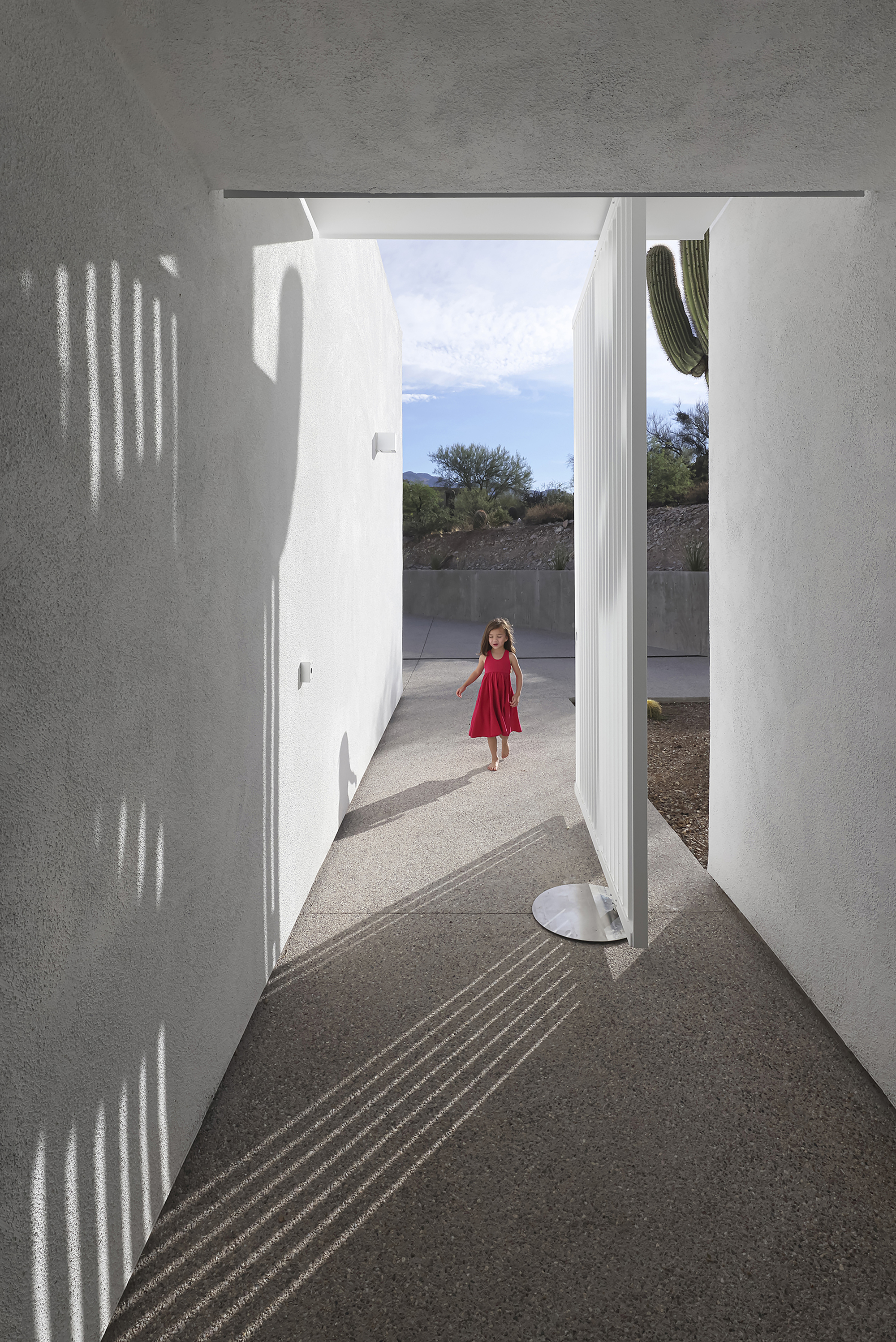 Entry corridor with patterned shadows from perforated screen and child standing in distant courtyard