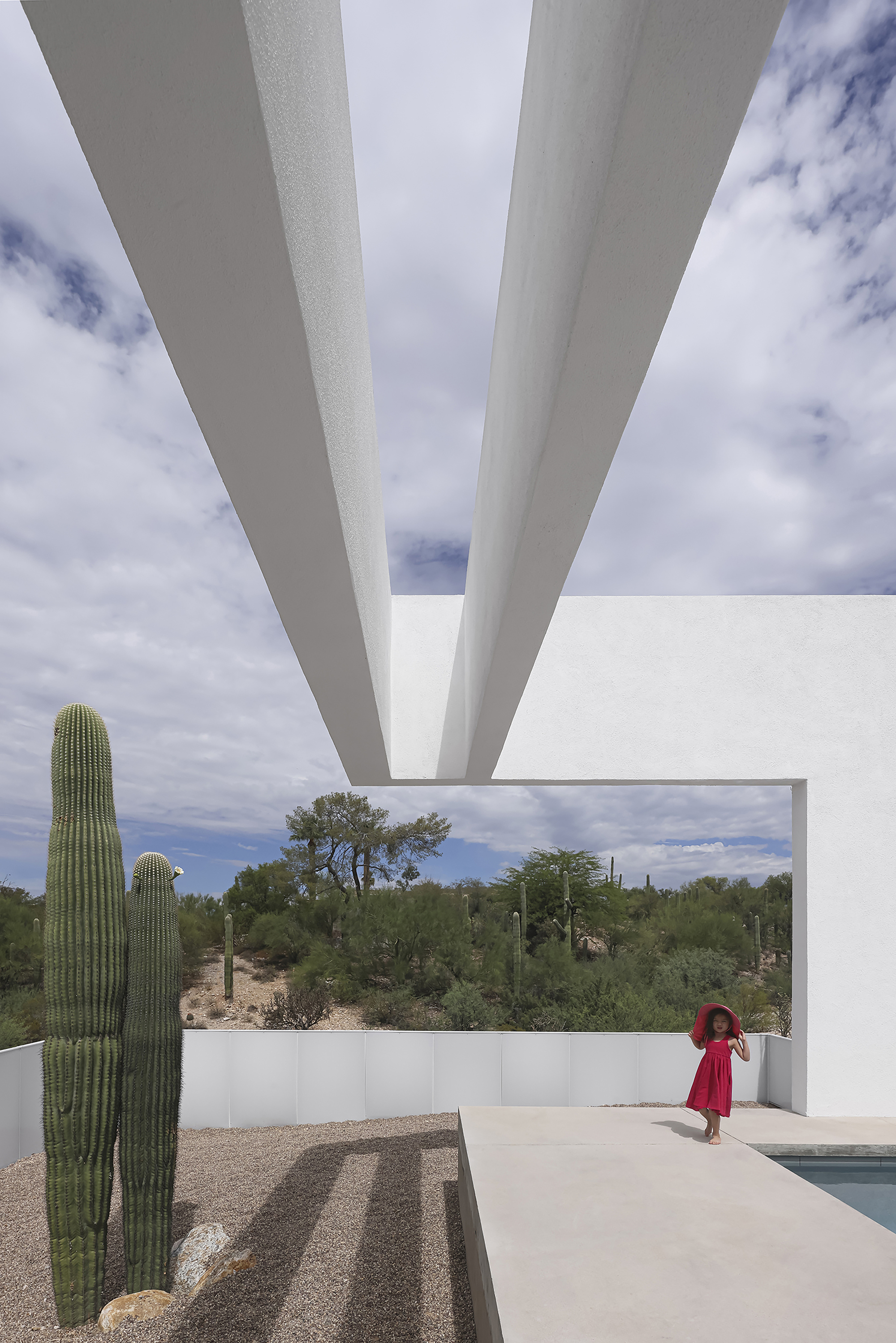 View beneath tapered white concrete roof beams overlooking the pool terrace and desert beyond